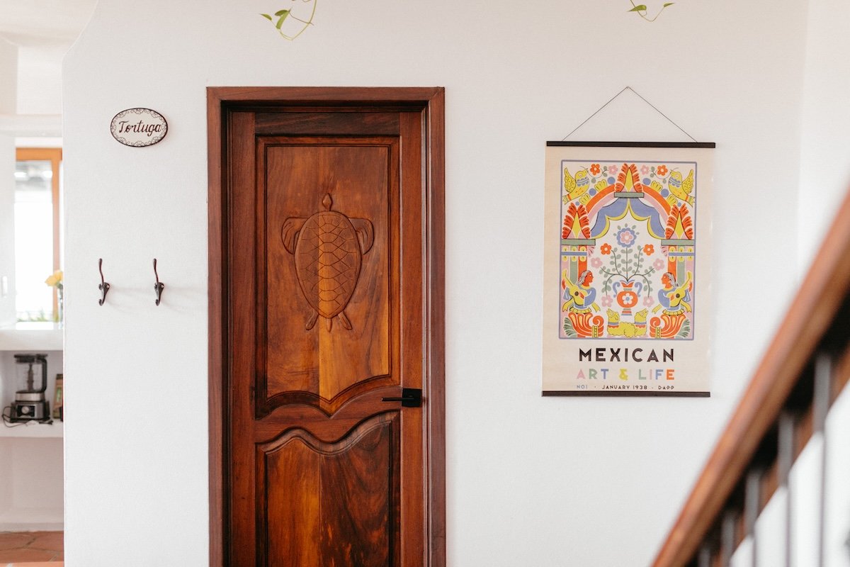 Decorative wooden door with turtle carving, next to a colorful Mexican art and life poster on a white wall.