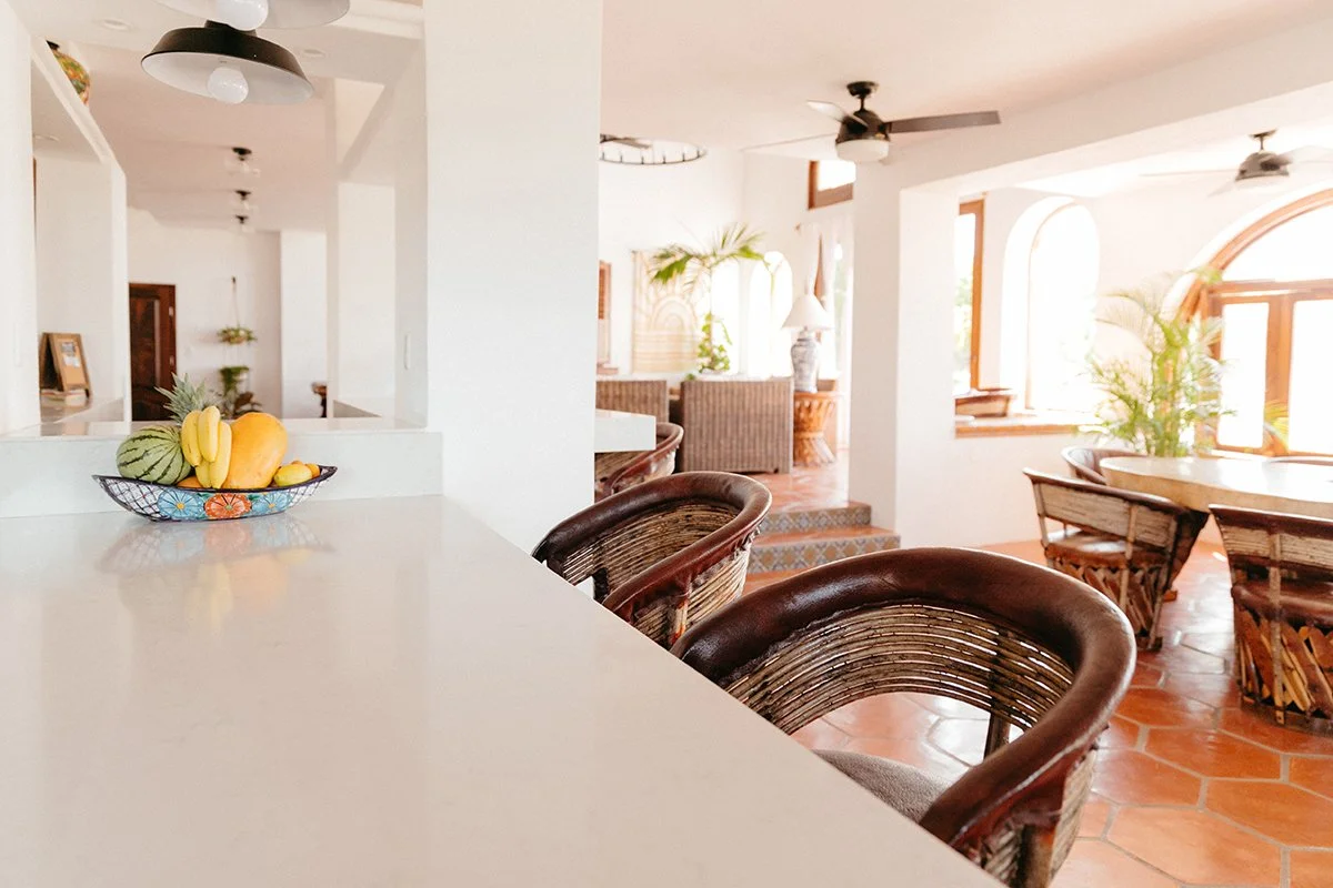 Bright and airy living area with wicker chairs, large windows, and tropical plants.