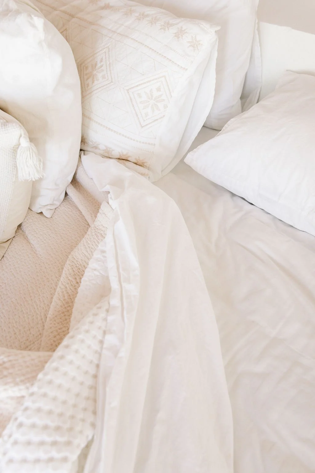 Close-up of a bed with white pillows and cream-colored bedding with embroidery.