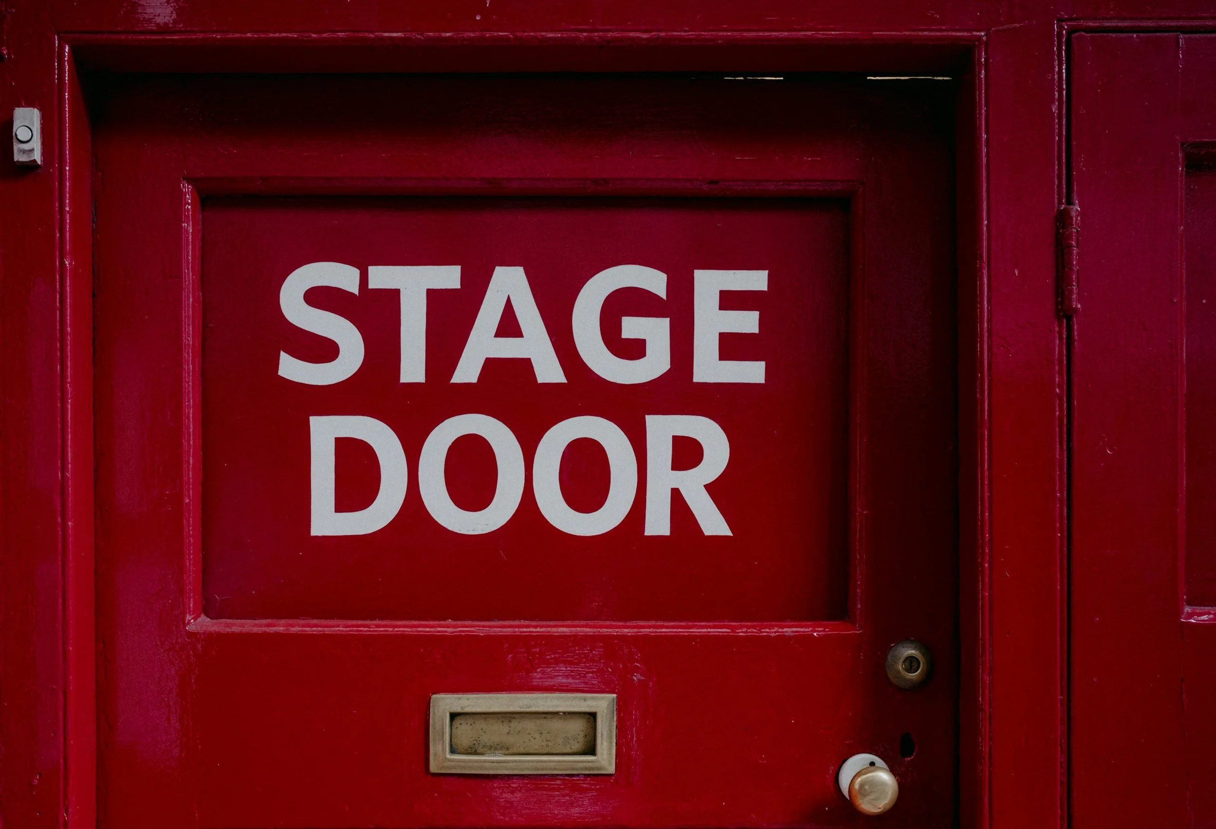 Red door with a sign reading "STAGE DOOR" in white letters.
