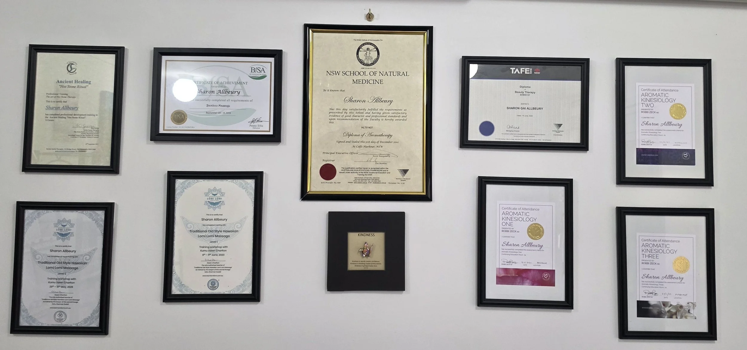 A wall display with multiple framed certificates and awards, including diplomas and achievement recognitions, arranged in a grid-like pattern.