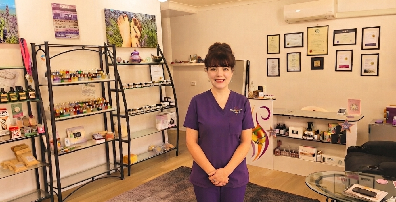 Woman in purple scrubs standing in a wellness shop with shelves of essential oils and health products.