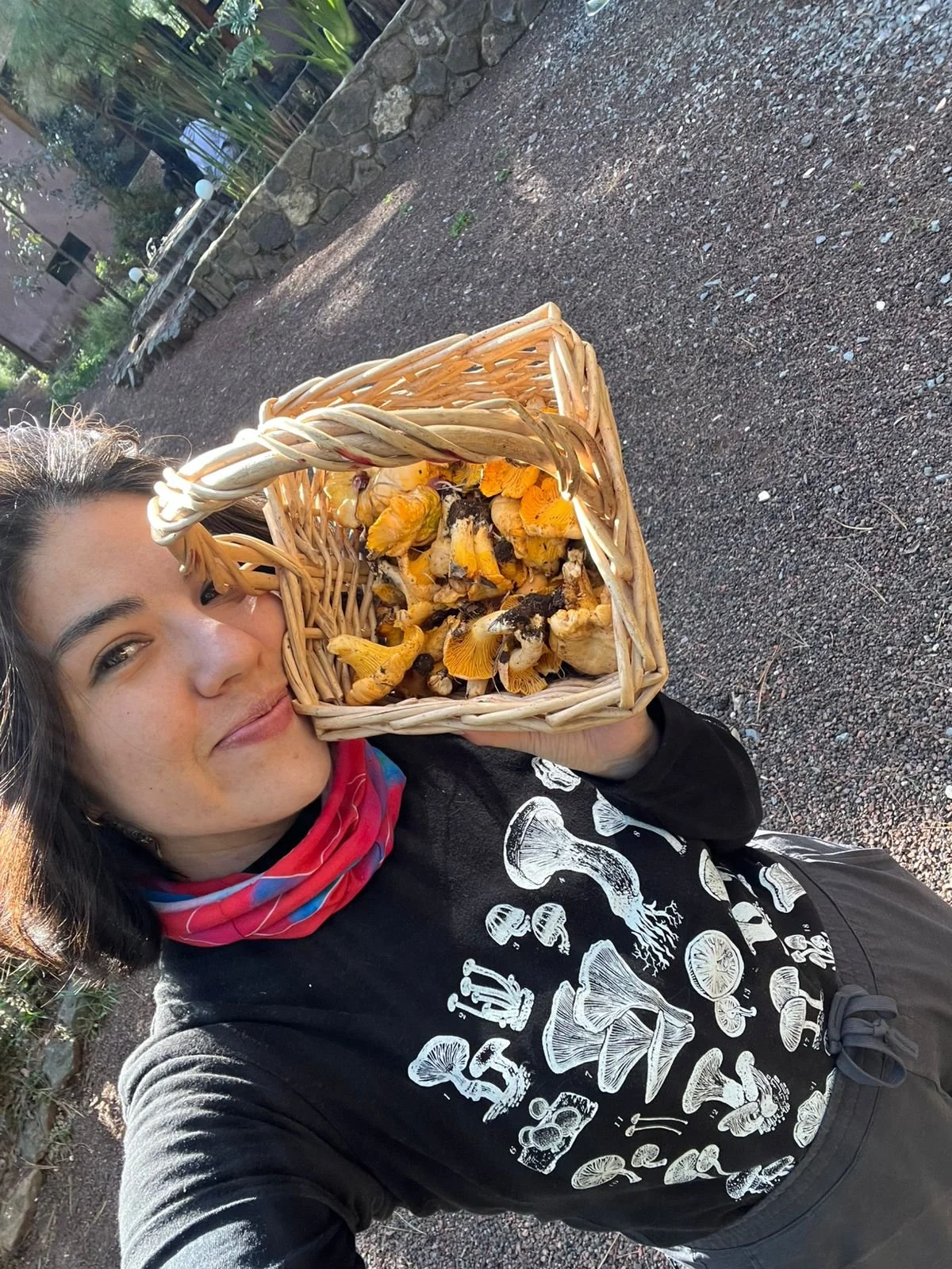 Mujer sonriente sosteniendo una cesta con setas comestibles en un entorno al aire libre.