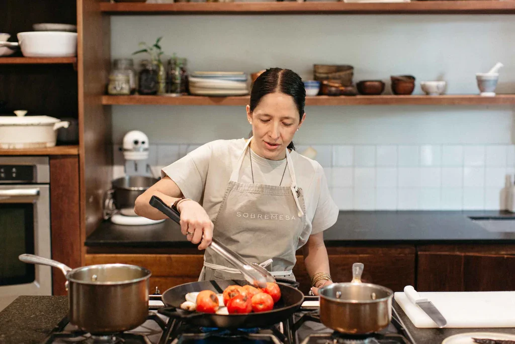 Una mujer cocinando en la estufa con tomates y otros ingredientes en la sartén en una cocina moderna. Sobremesa