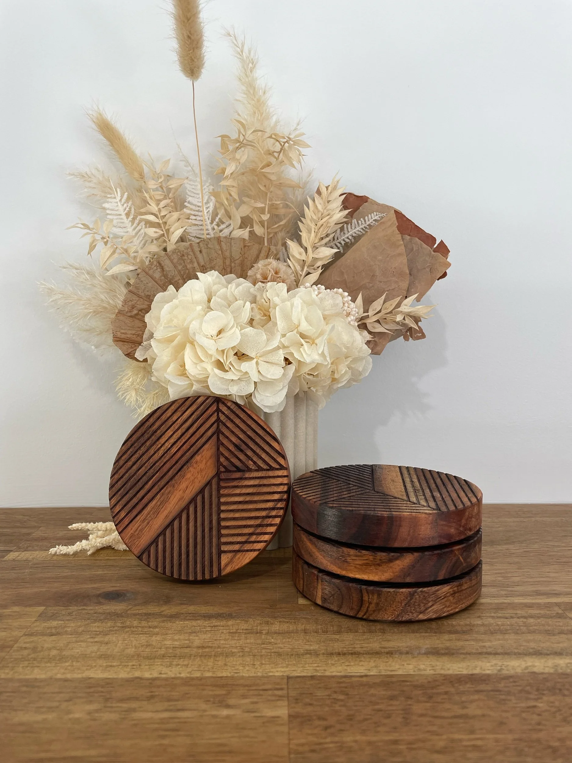 Arrangement of dried flowers in neutral tones on a white background, with wooden decorative pieces on a wooden surface.