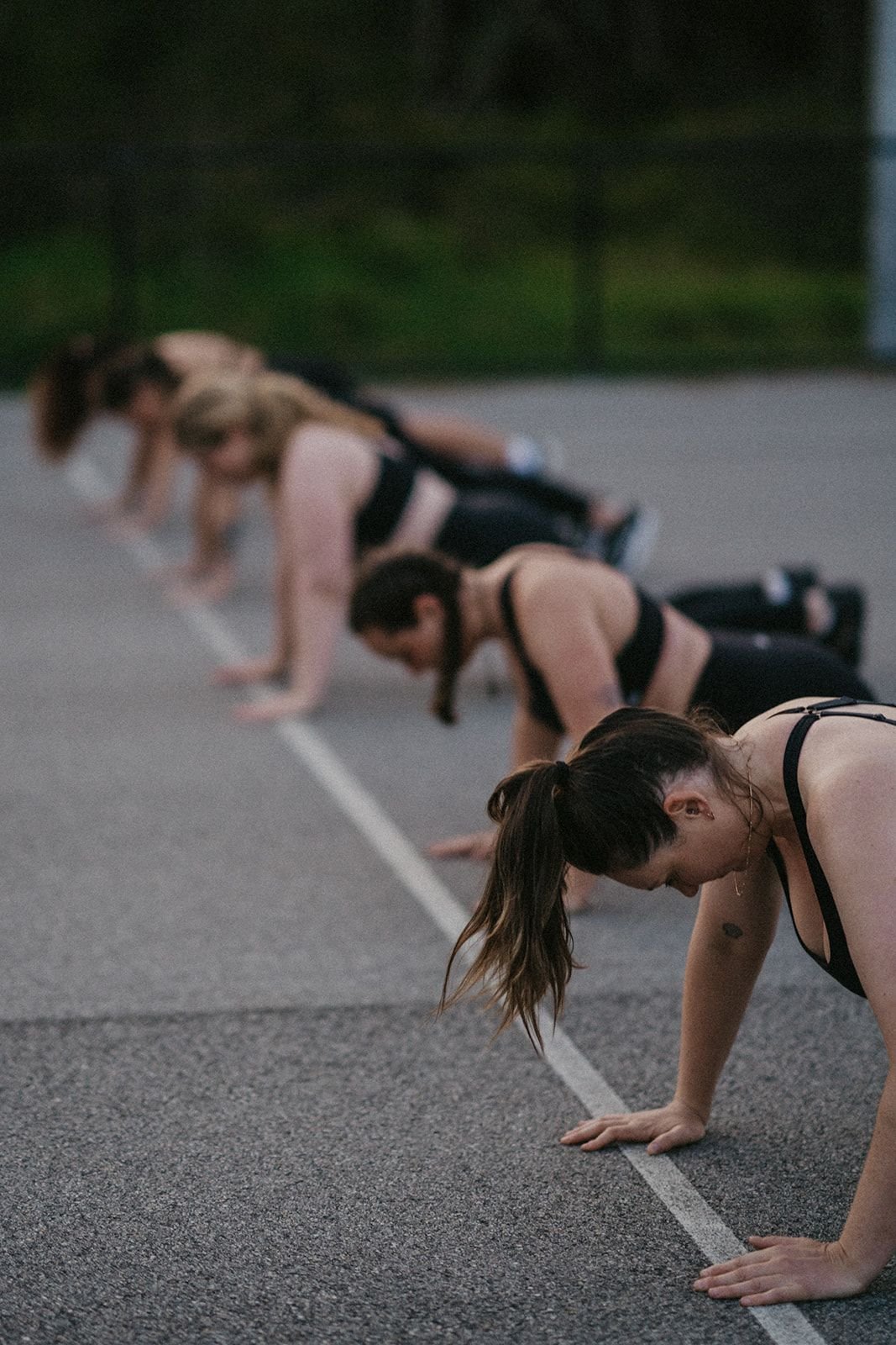 Group of women in workout clothes doing planks on a running track during sunset.