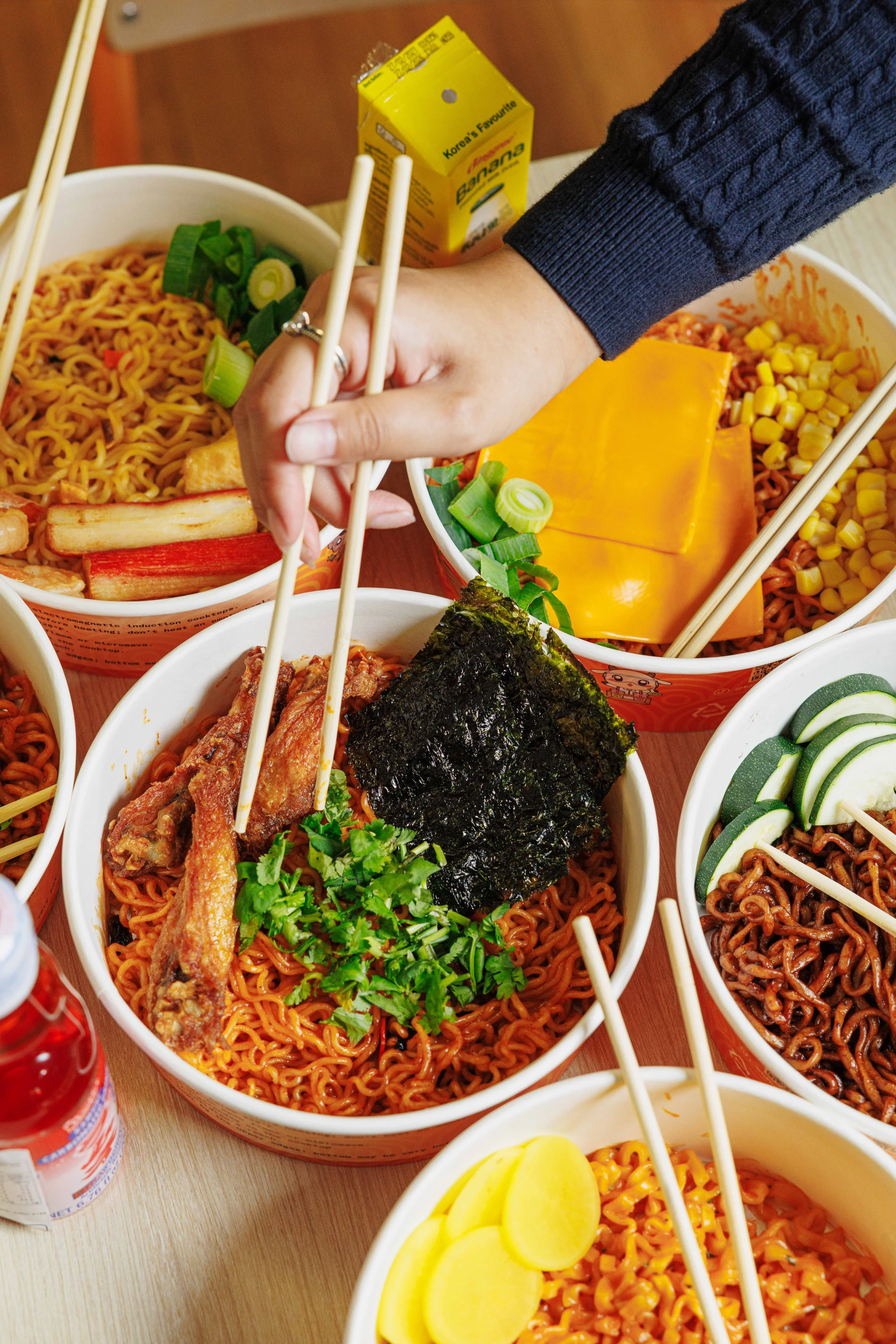 Assorted Korean instant noodles in bowls topped with vegetables, seaweed, and sliced pickled radish, with chopsticks resting on each bowl.