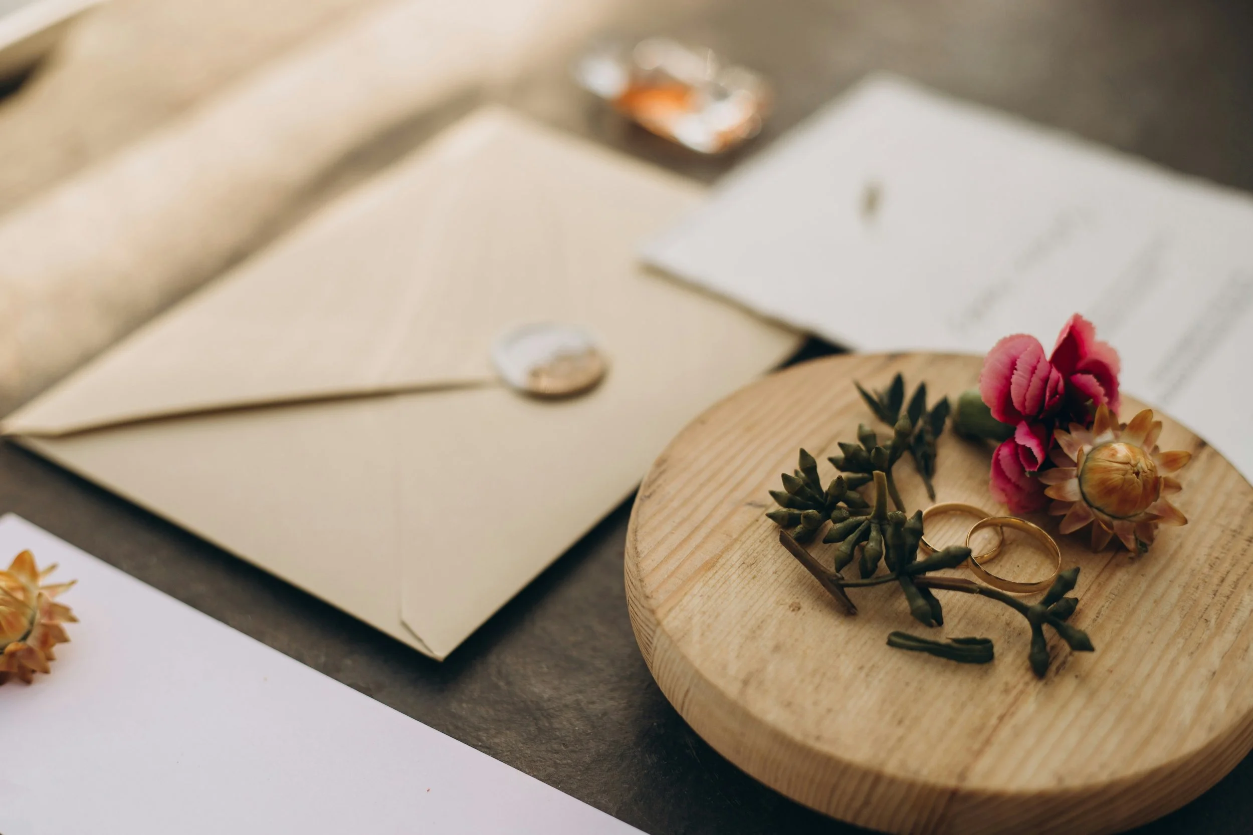 Delicate wedding rings and fresh pink florals on a timber styling board for an intimate Central Coast celebration.