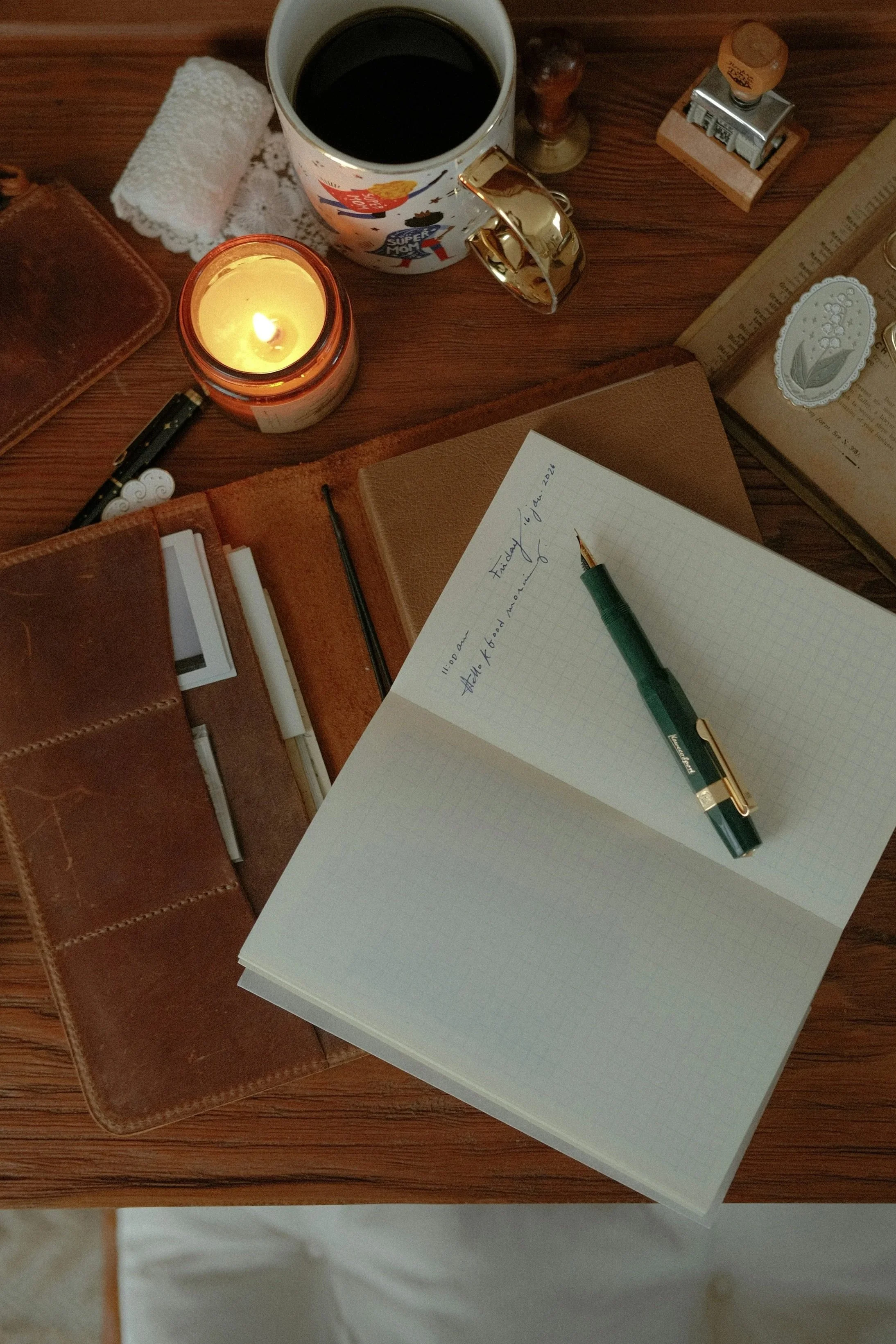 A moody flatlay wedding planning workspace with a notebook, leather journal, and lit candle in the Hawkesbury.
