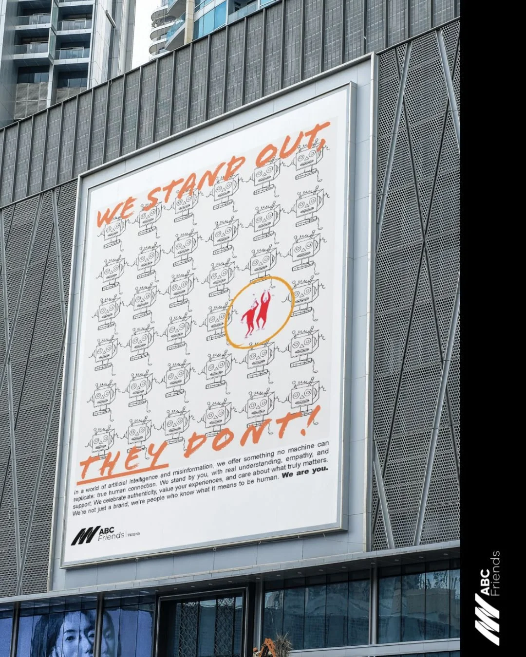 A large billboard with the message 'We stand out, they don't!' featuring cartoon drawings of robots and a central illustration of two human figures hanging from a hook, set against a city building background.