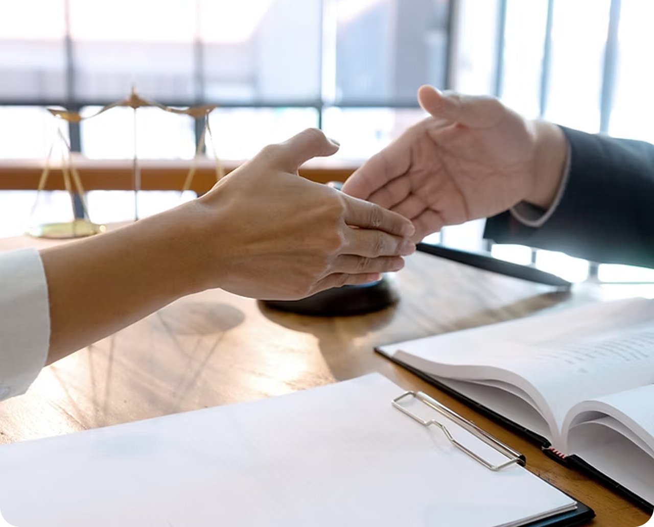 Two people shaking hands at a table in an office or conference room.