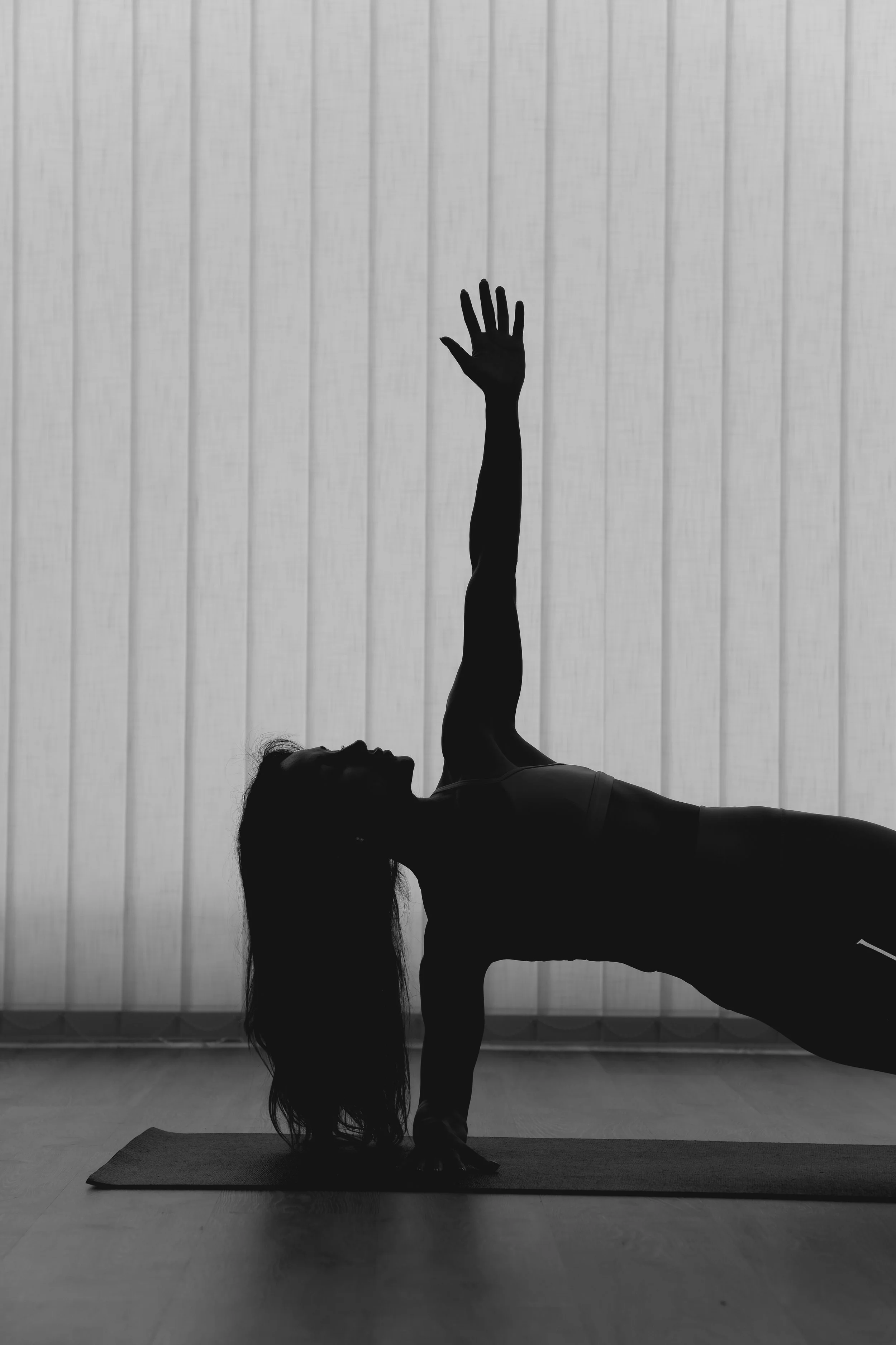 A person practicing yoga indoors, performing a pose on a yoga mat in front of a semi-transparent window.