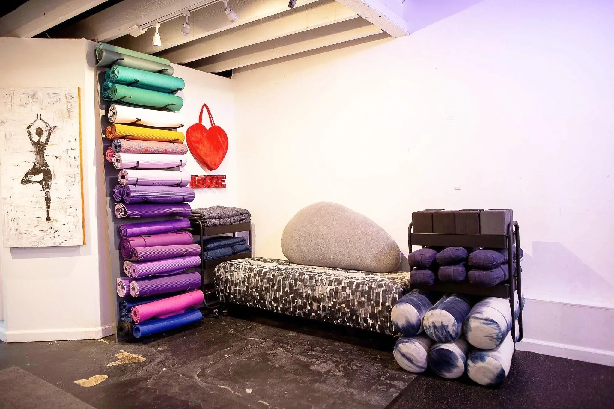 Yoga mats in various colors leaning against the wall, a large heart-shaped decoration.