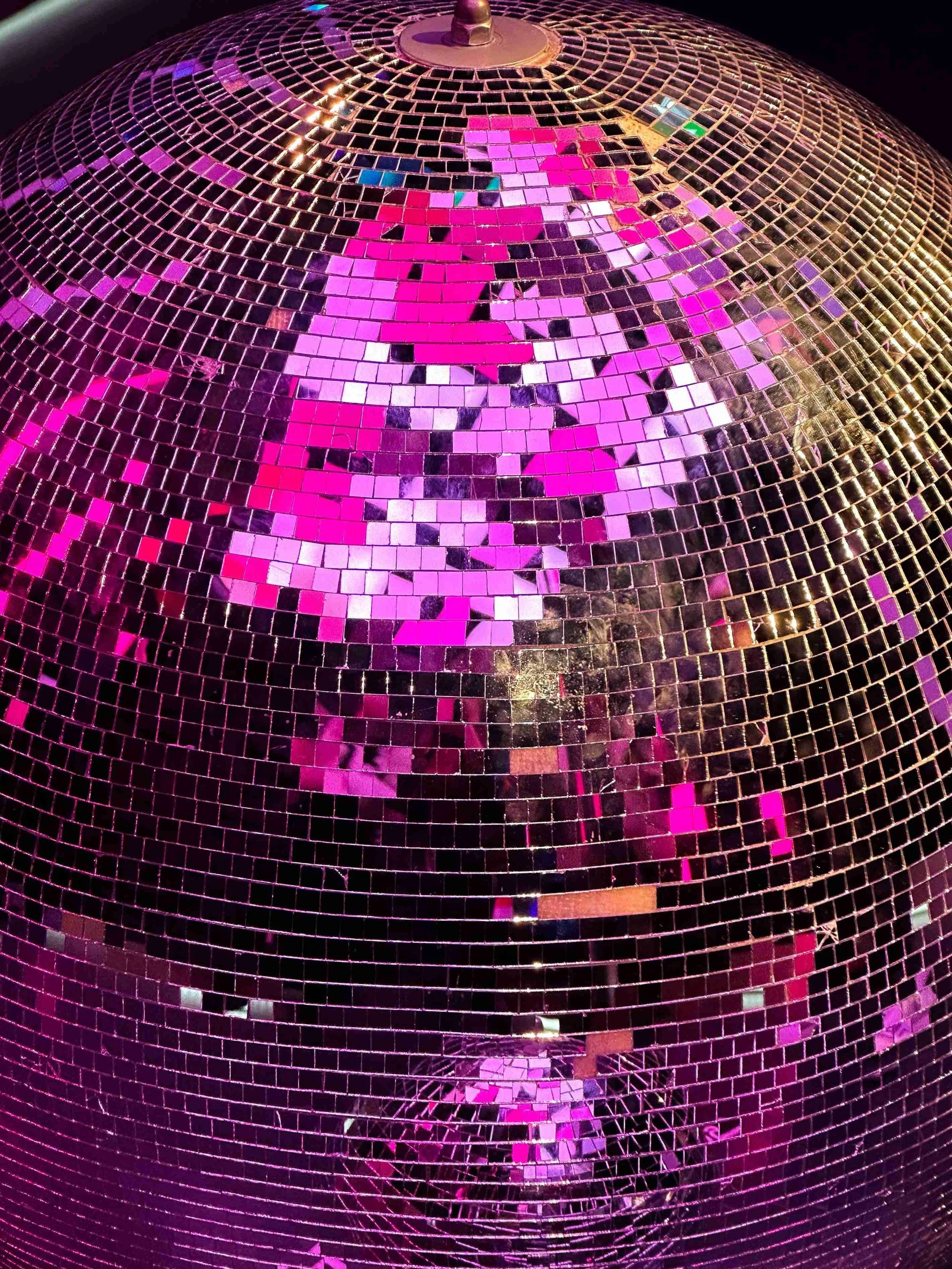 Close-up of a spherical disco ball with pink and purple tiles reflecting light against a dark background.