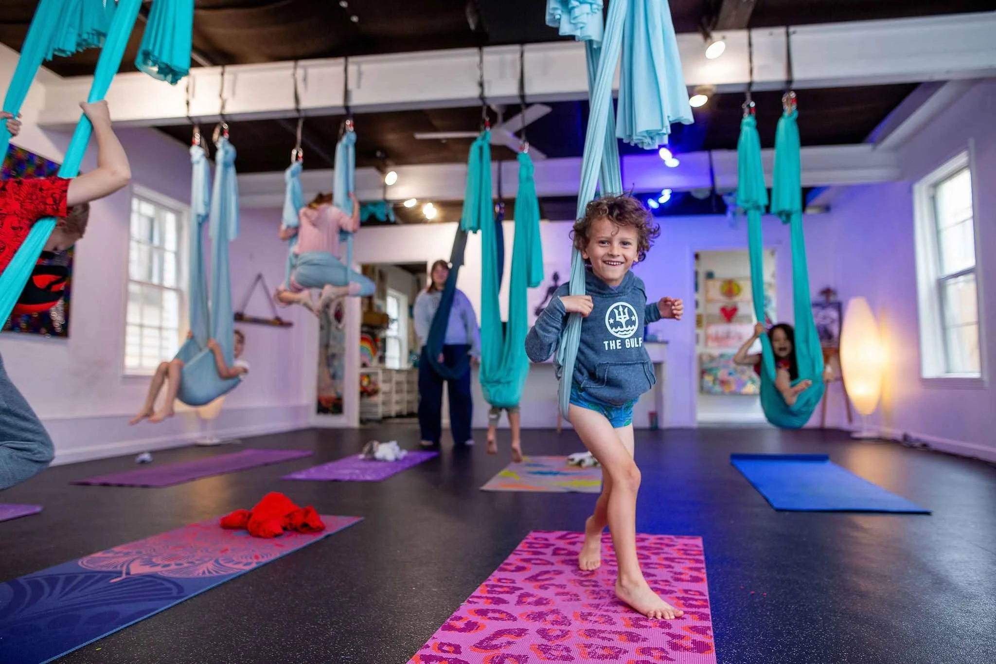 Children practicing aerial yoga with fabric hammocks in a colorful indoor studio.