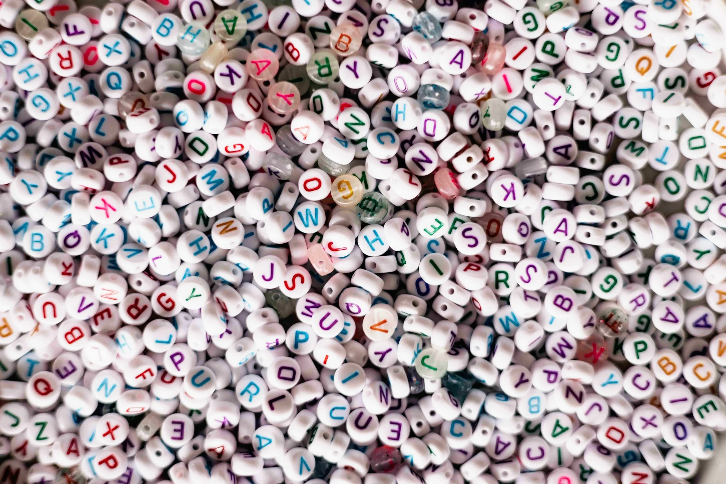 A large pile of small white beads with multicolored letters on them.