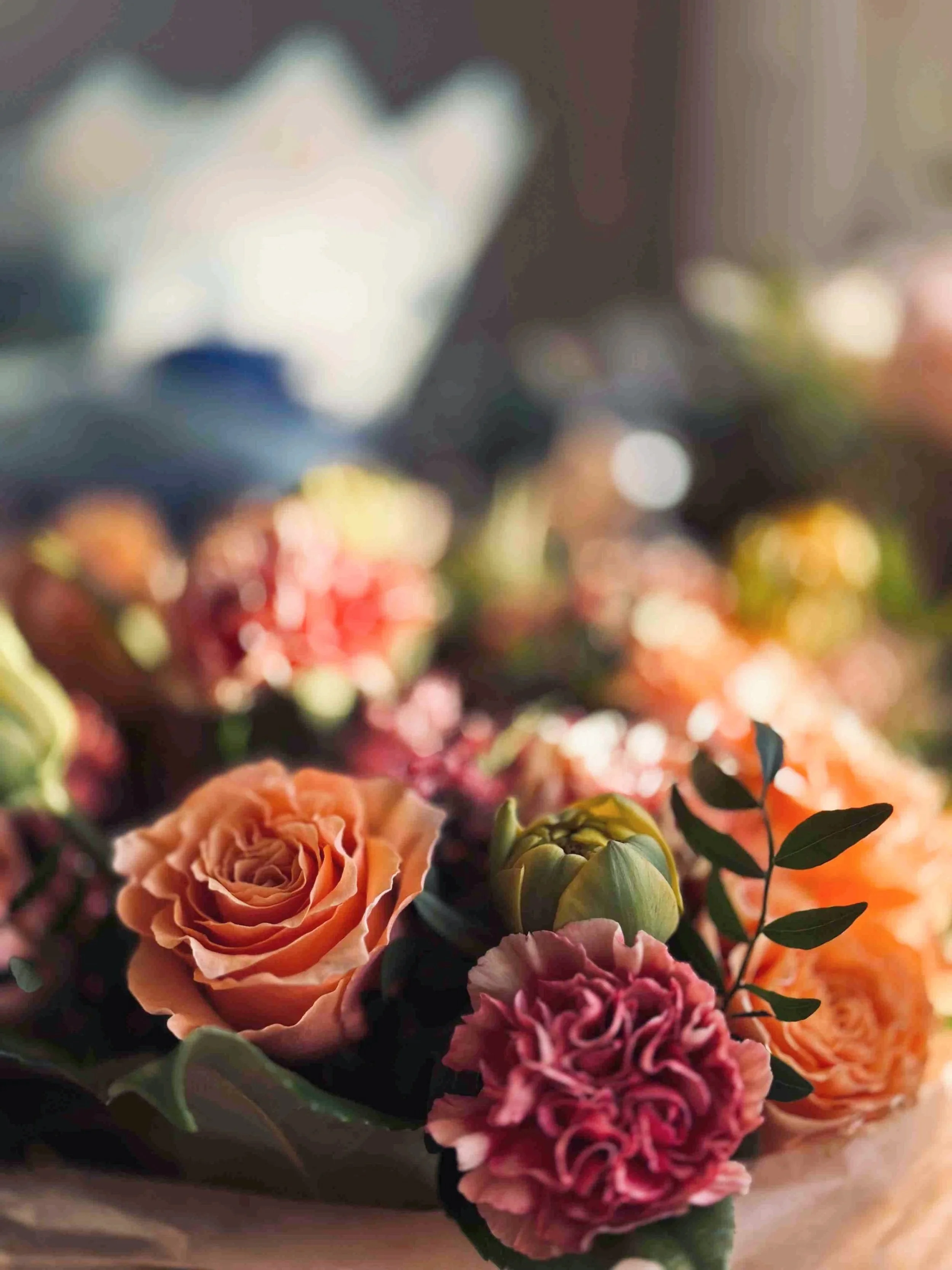 Close-up of a bouquet of orange roses, pink carnations, and green leaves with a blurred background.