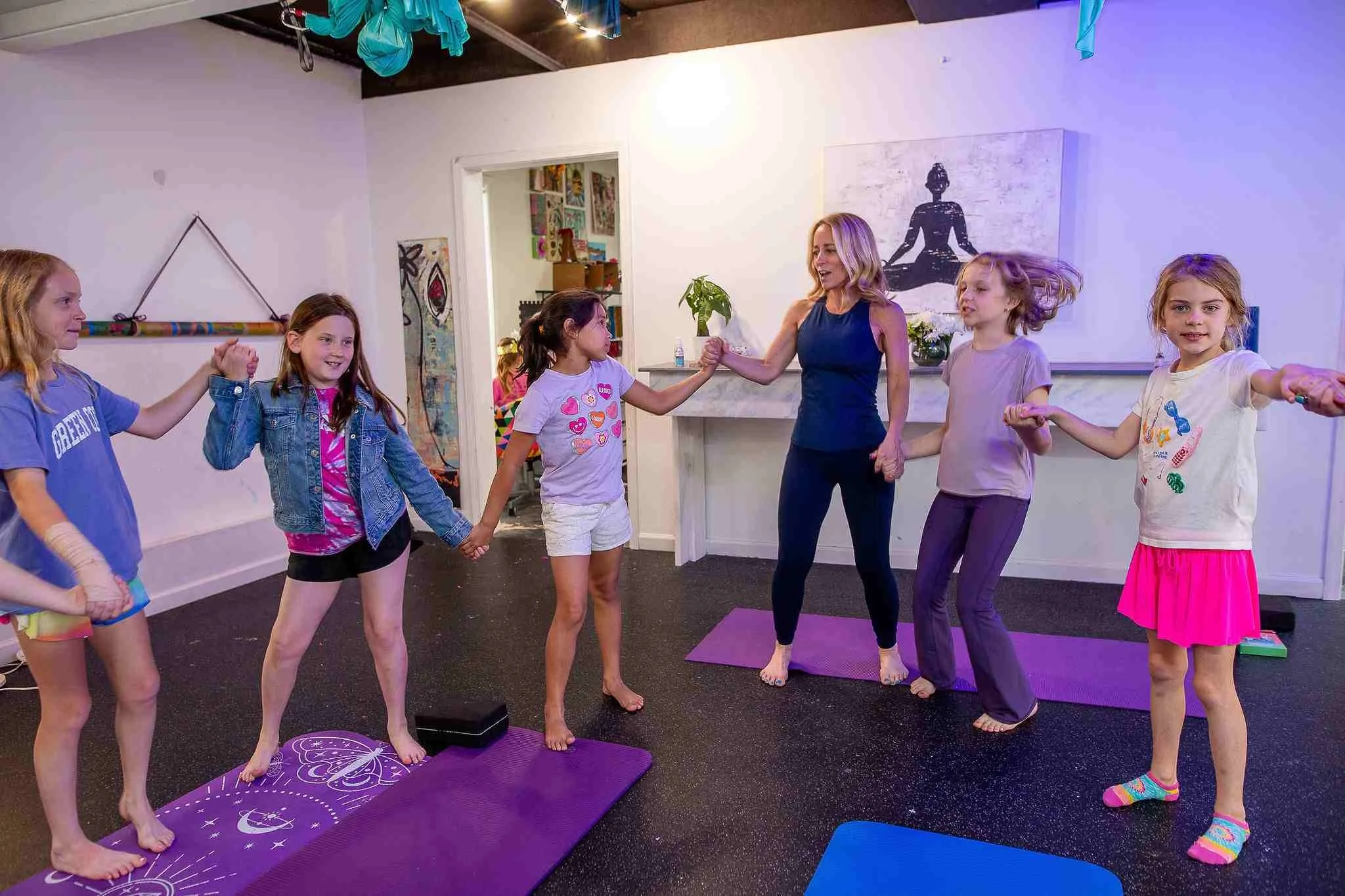 A group of children holding hands in a circle with an adult in a yoga studio.