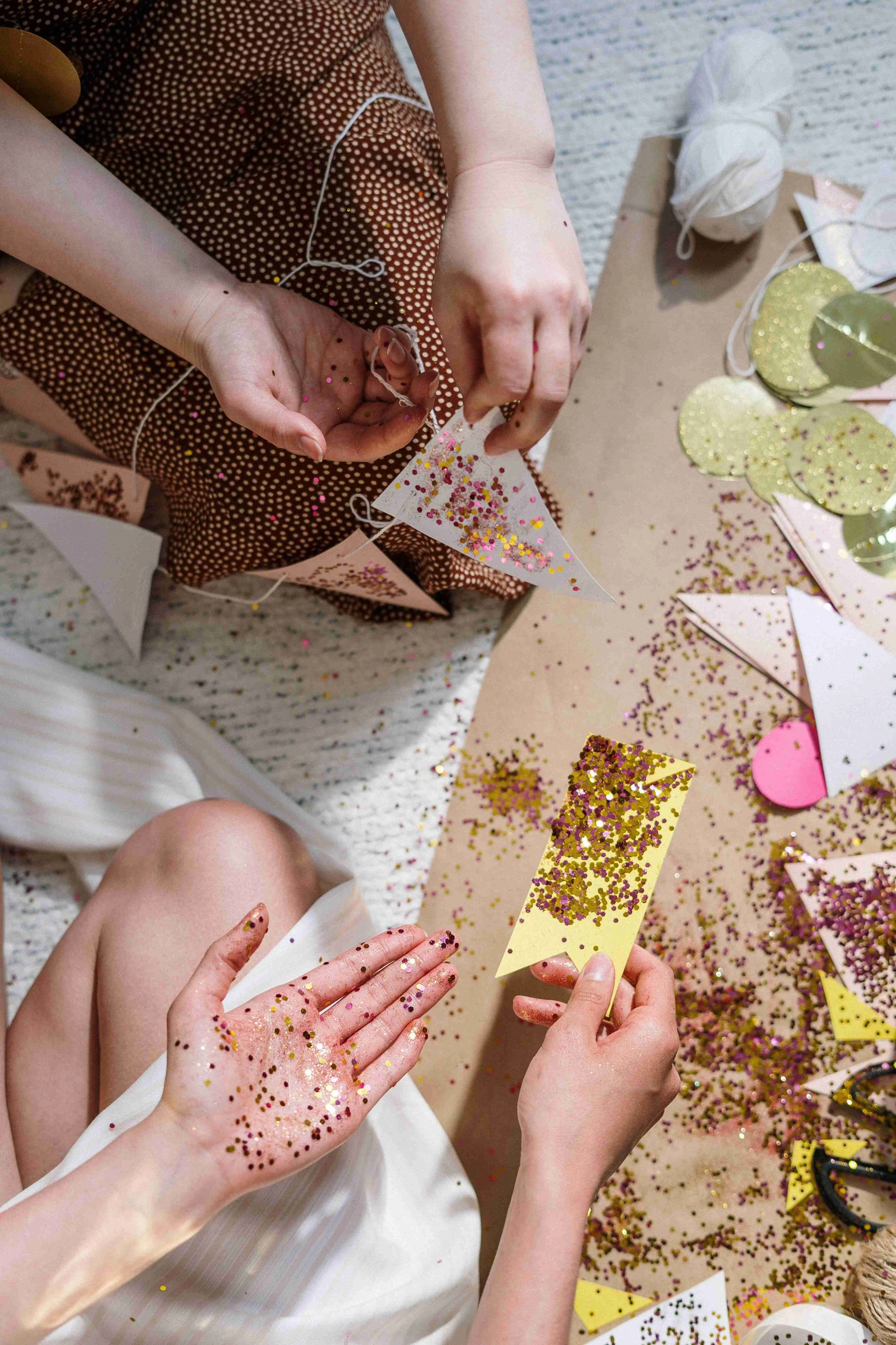 People celebrating with gold and pink confetti, glitter on hands, and colorful decorations, possibly at a party or festive event.
