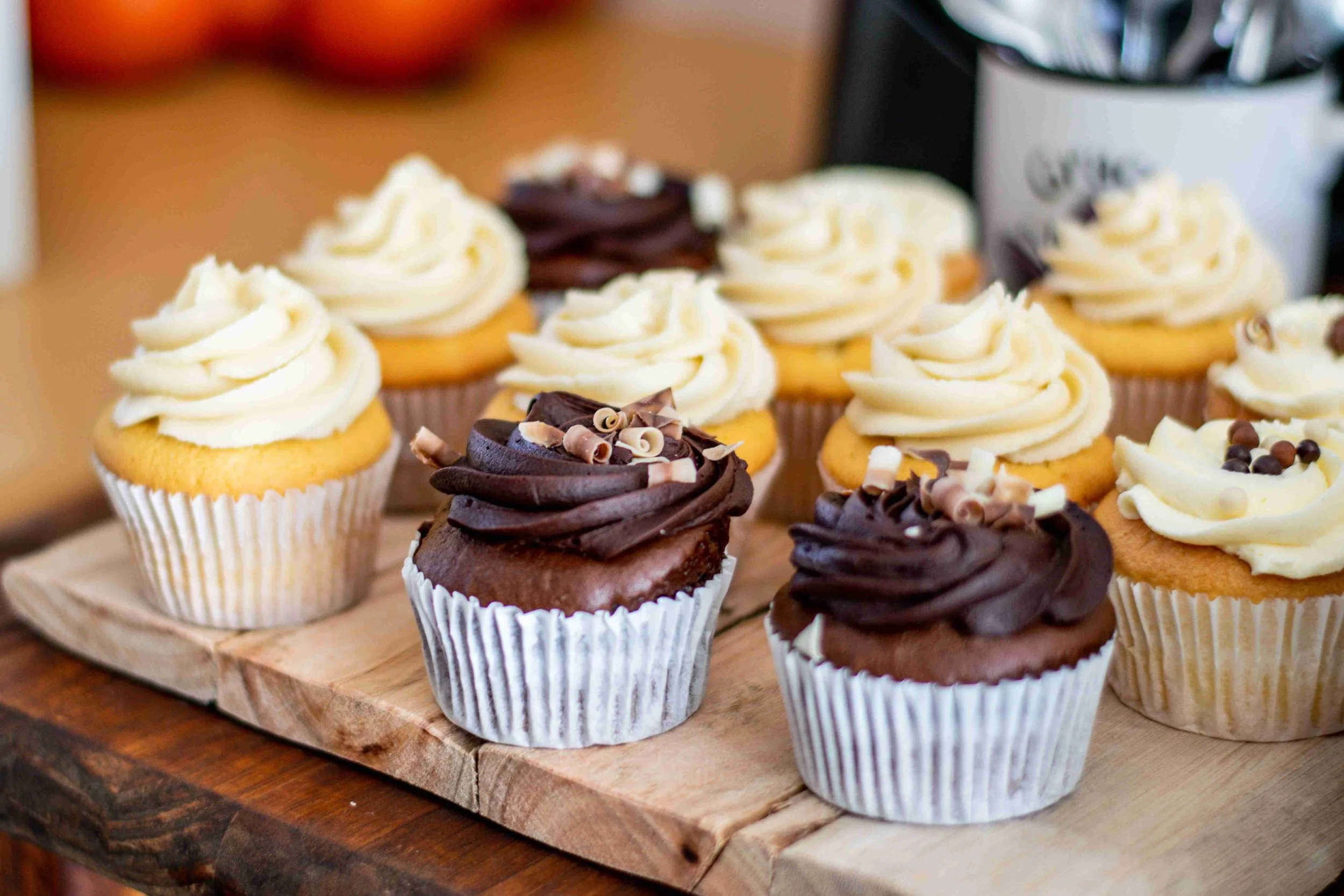 Assorted cupcakes with white and chocolate frosting topped with chocolate shavings, arranged on a wooden board.