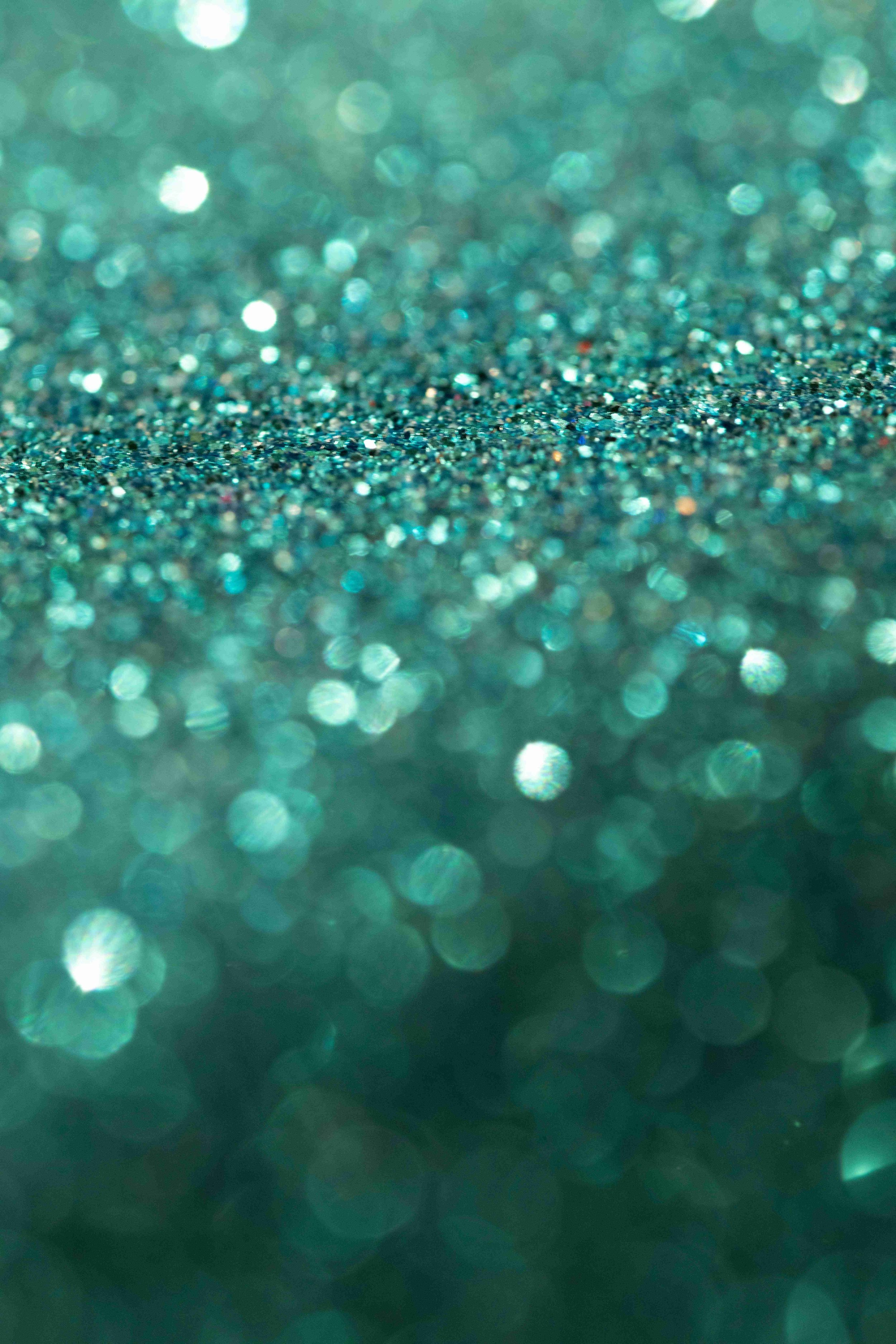 Close-up of glittering blue and green bokeh lights with a glitter surface in the foreground.