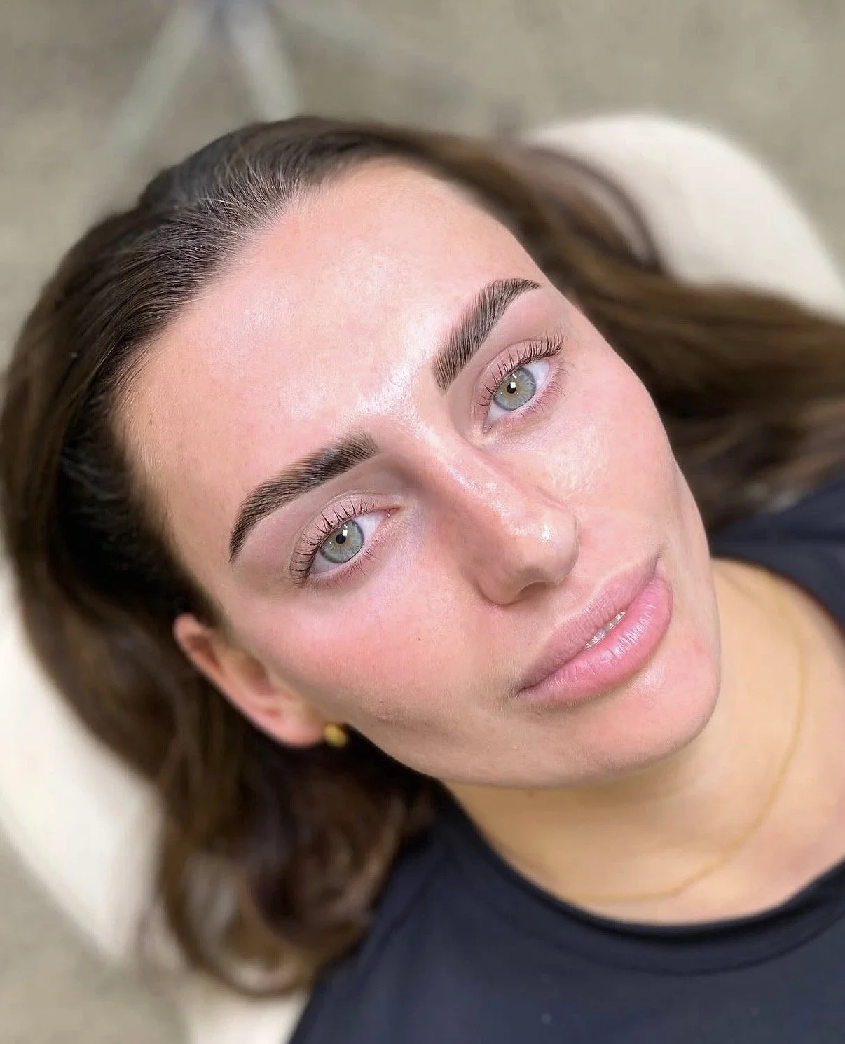 Close-up of a woman with light skin lying down, showing her face with groomed eyebrows, light eyes, and full lips.