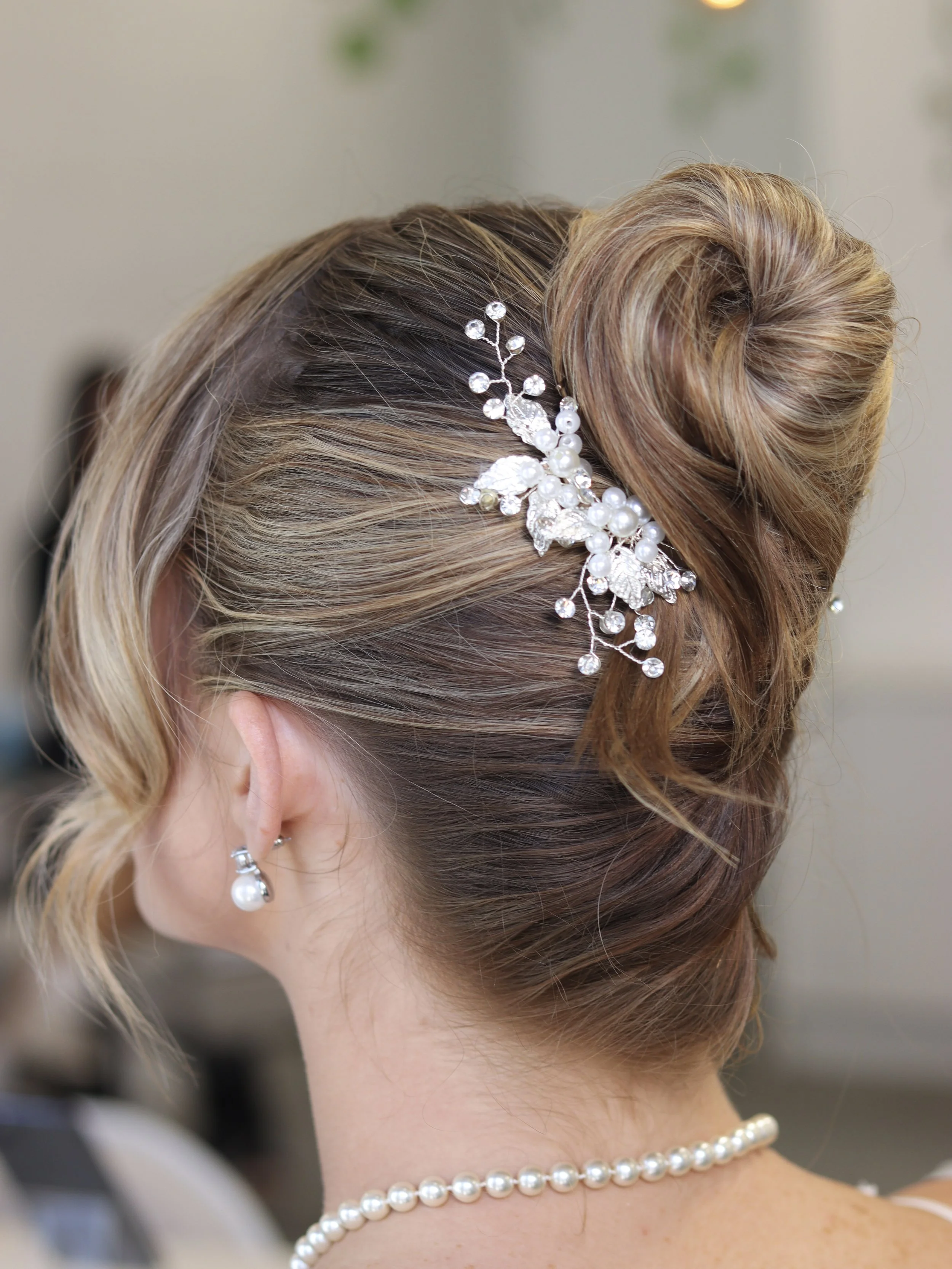 Close-up of a woman’s elegant hairstyle featuring a pearl and rhinestone hair accessory, with her hair styled in an updo and wearing pearl jewelry.