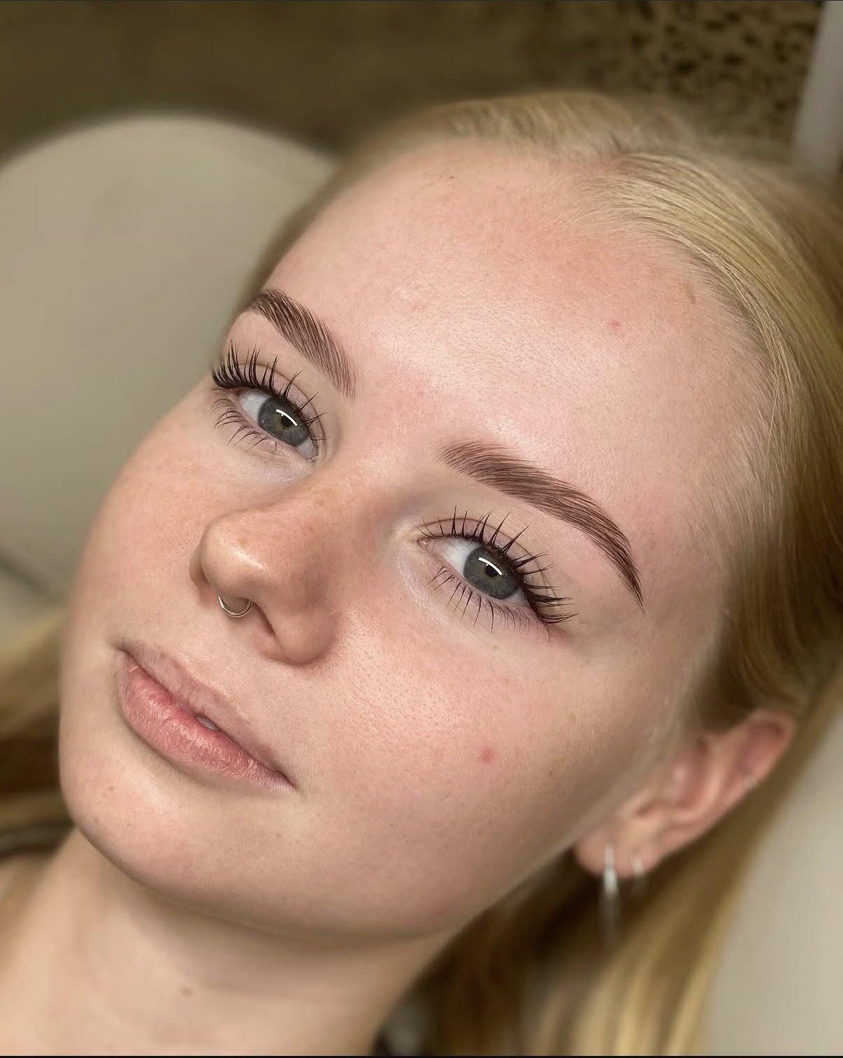 Close-up of a woman's face with well-groomed eyebrows, long eyelashes, and light skin freckles, lying down with a neutral expression.