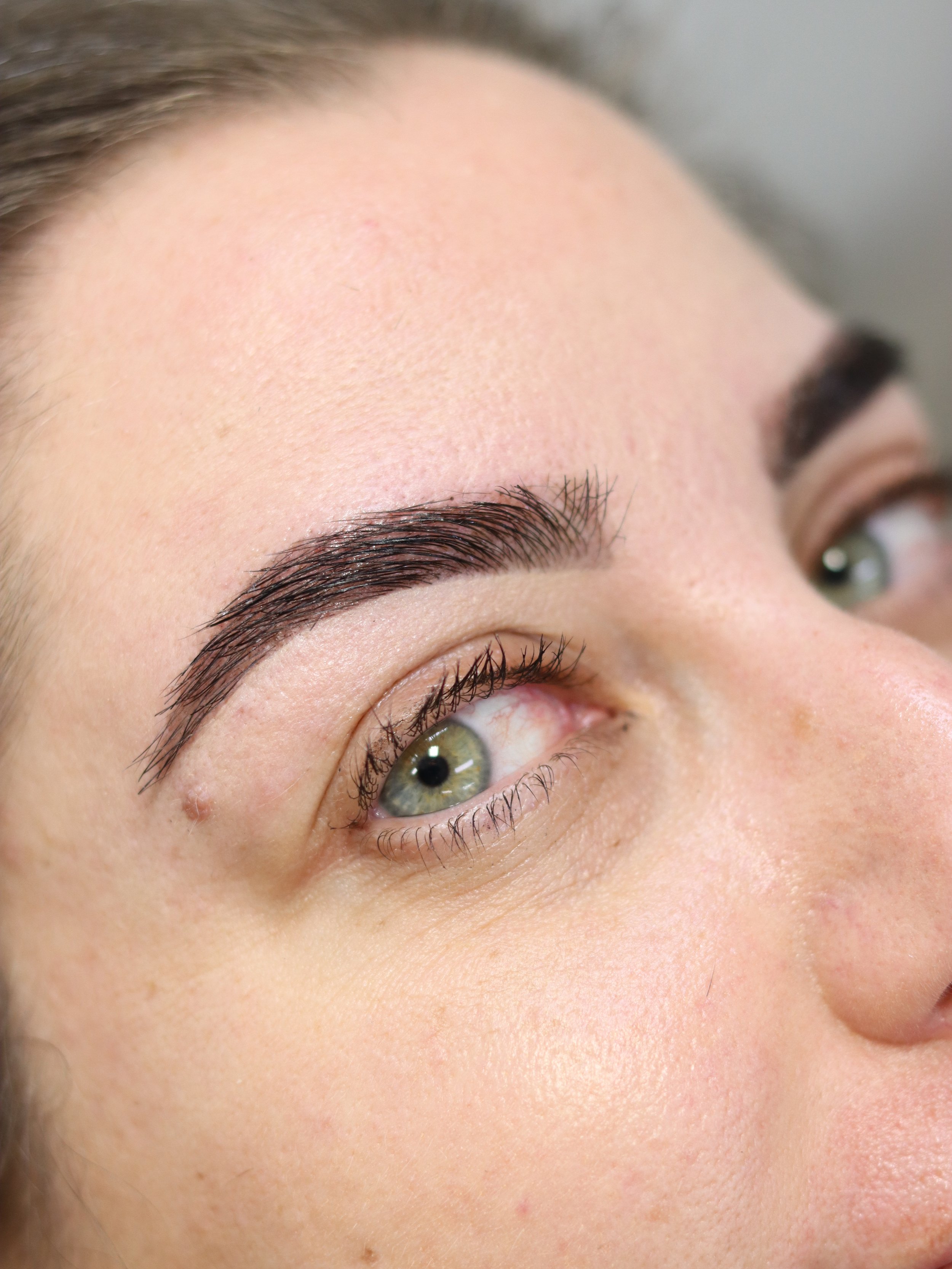 Close-up of a woman's face focusing on her right eyebrow, eye, and forehead, with light skin and natural makeup.