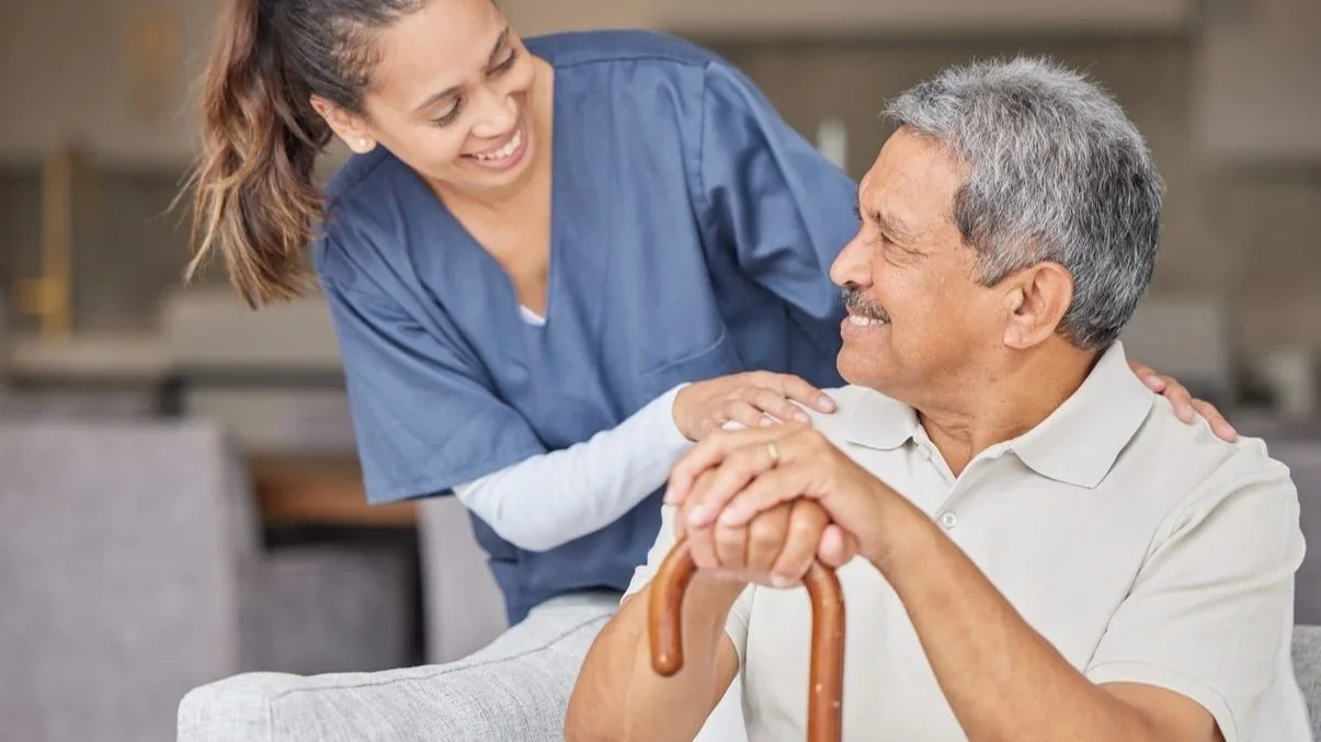 Nurse smiling and interacting with an elderly man holding a cane, in a healthcare setting.