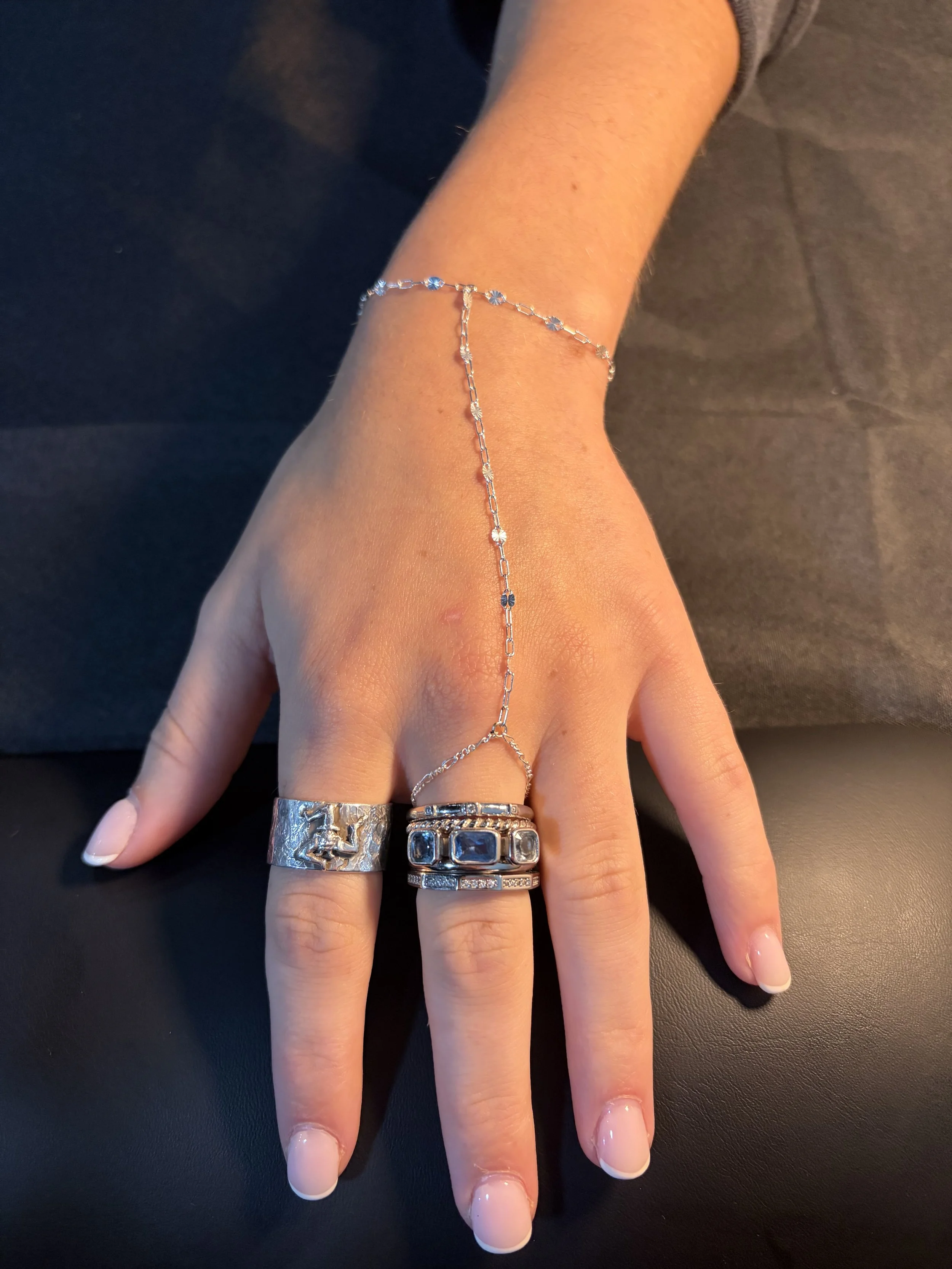 A hand resting on a black surface, wearing multiple silver rings and a delicate bracelet with small gemstones.
