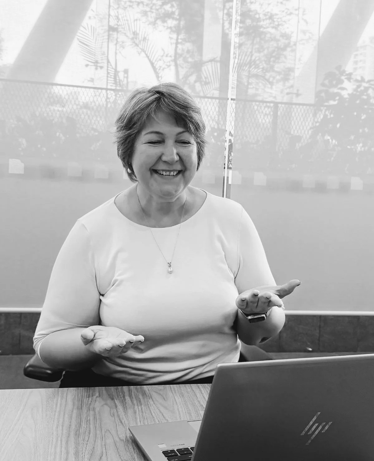 Black and white photo of Sasha Kitashova, coach and coach supervisor, sitting infront of a laptop. She is talk and using her hands to describe a concept while on a video conference call. 