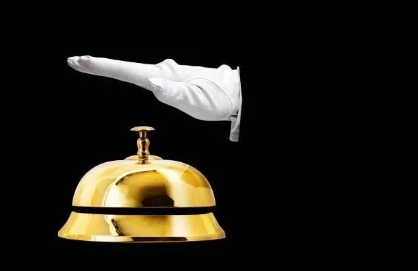 A white-gloved hand pointing at a gold service bell against a black background.