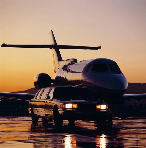 A private jet aircraft on a wet tarmac at sunset, with a limousine parked in front.