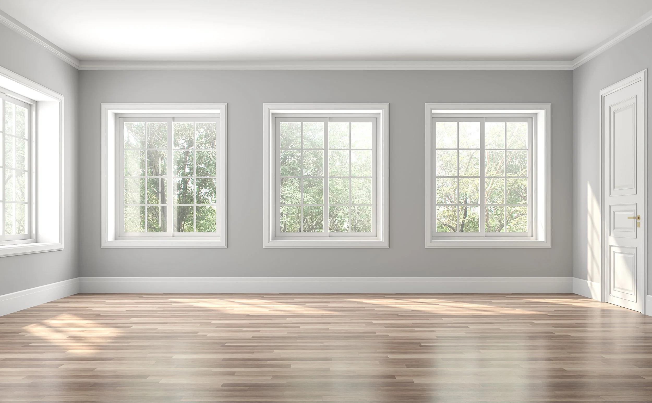 Empty room with three large windows, the windows are the show concept. Showing greenery outside, light gray walls, white trim, and a wooden floor.