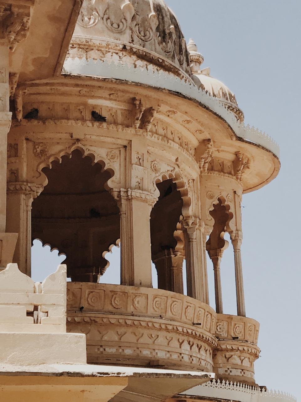 Close-up of an ornate, historic marble building with detailed carvings and latticework, featuring domed roof elements and arched openings in a warm stone color.