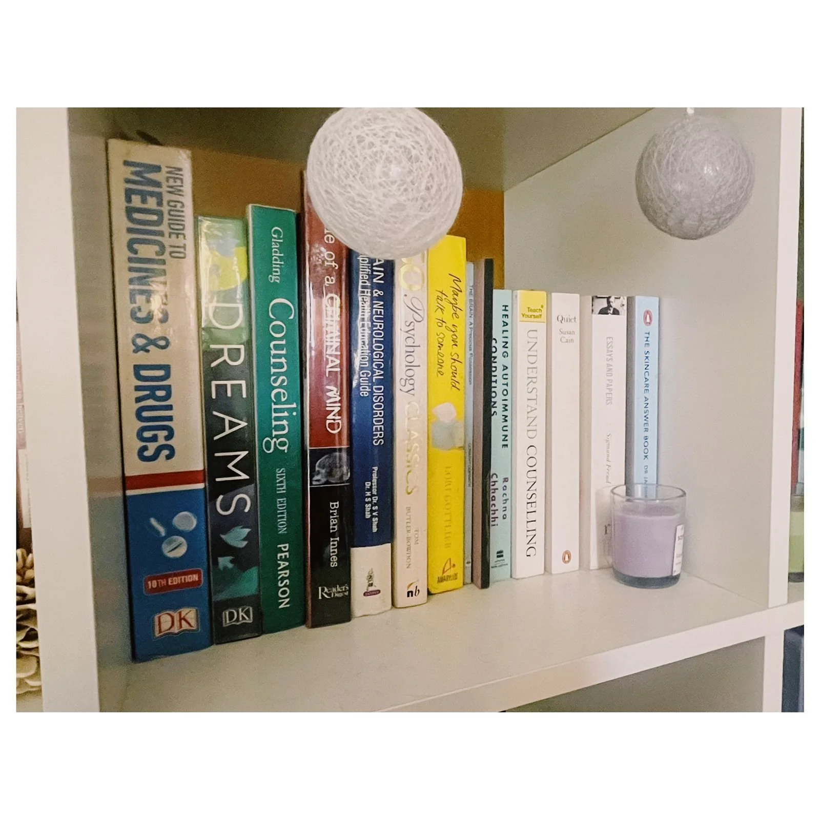 Bookshelf with various books, a spherical string light, and a small candle holder on the right.