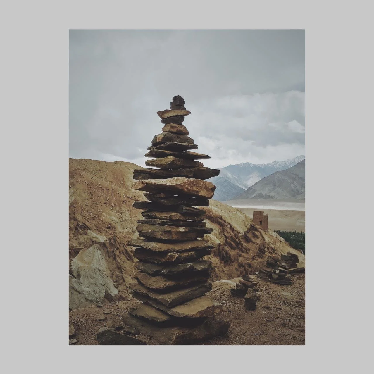 A tall stack of flat stones arranged in a balanced formation against a mountainous landscape with cloudy sky.