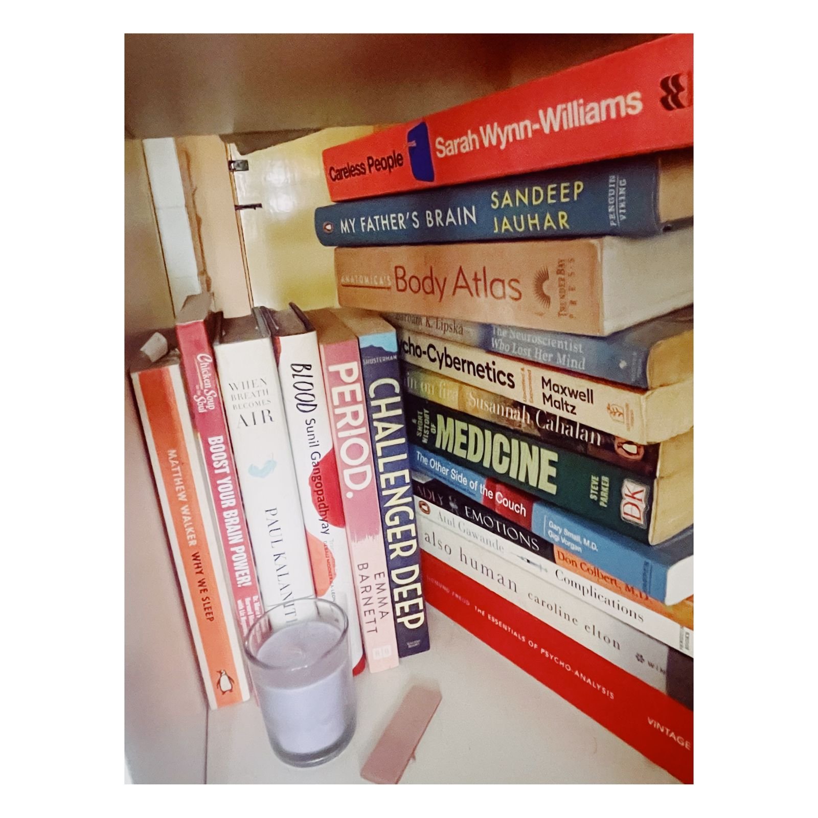 Stack of books on psychology and human behavior with a glass of water in front.