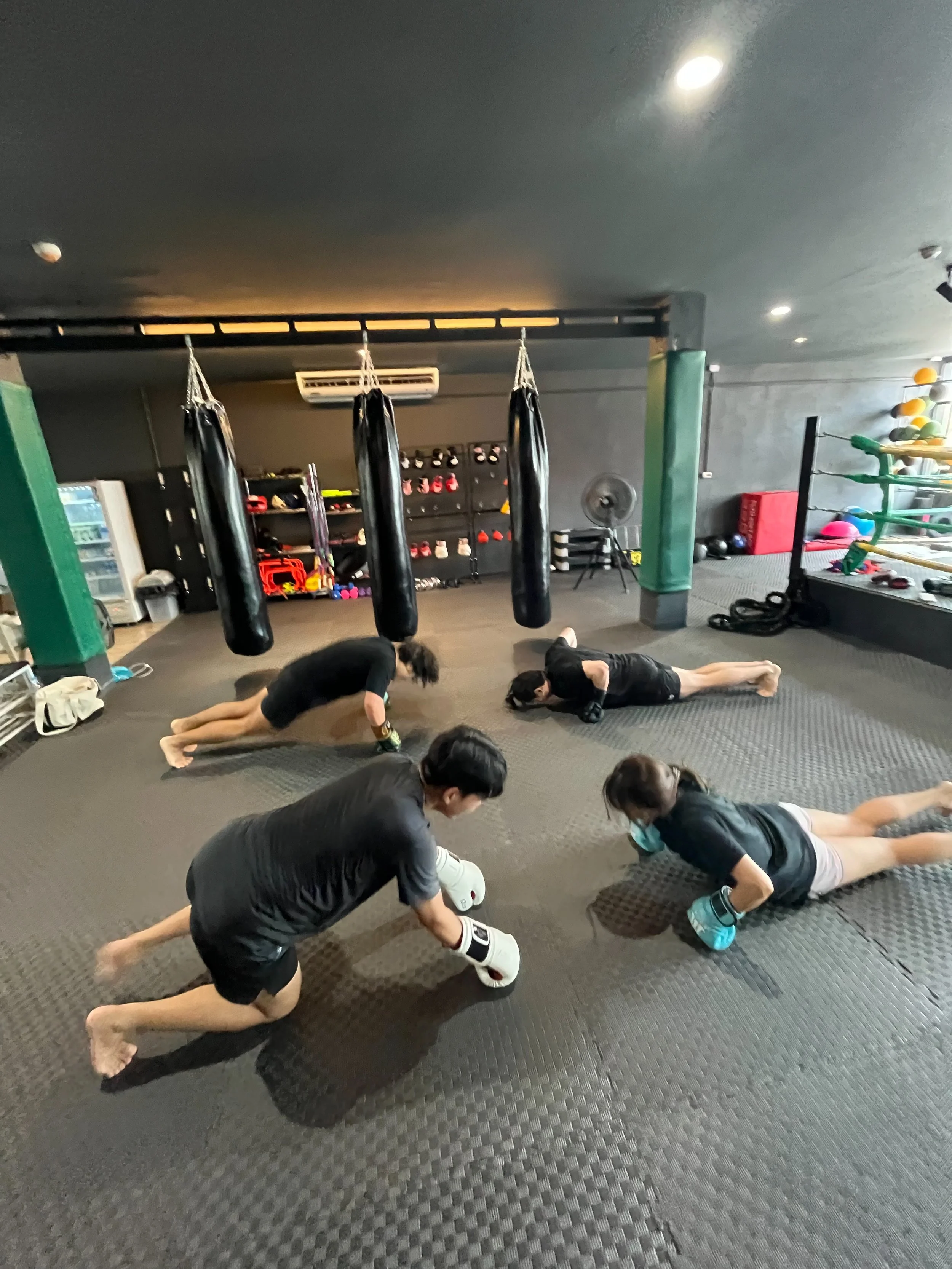 Group of people in a gym practicing stretching exercises on black mats.