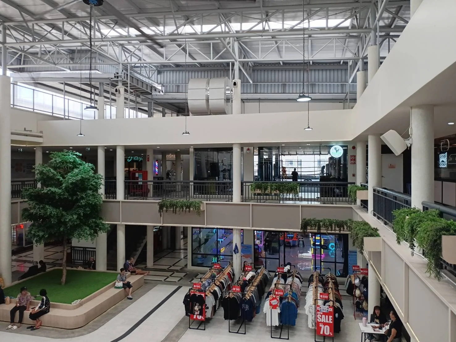 Interior of a shopping mall with a clothing sale display, seating area with people, Ranger Boxing Gym can be seen on the second floor.