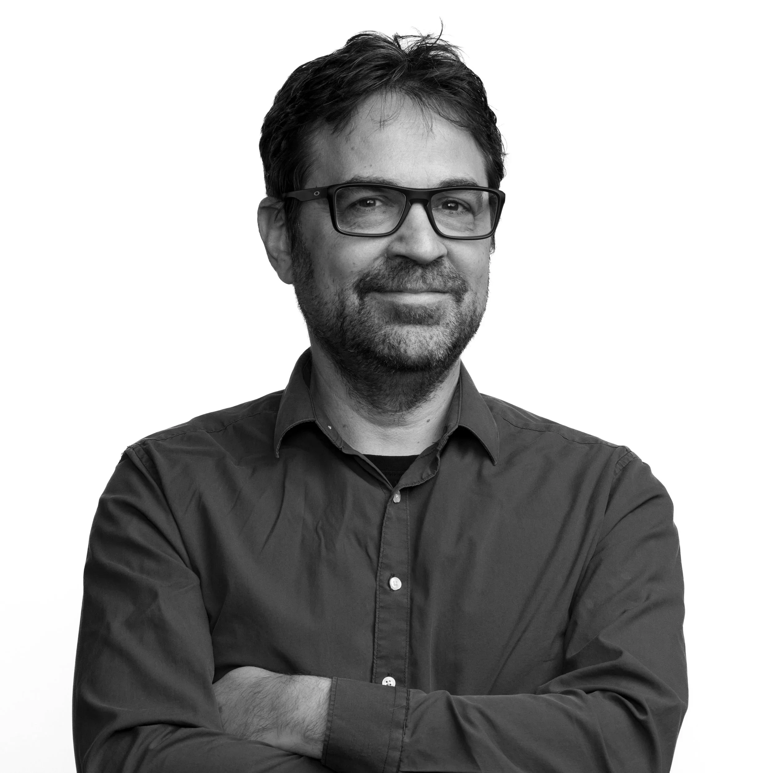Black and white portrait of a man with dark hair, glasses, a beard, and a mustache, smiling slightly, wearing a dark shirt against a plain background.