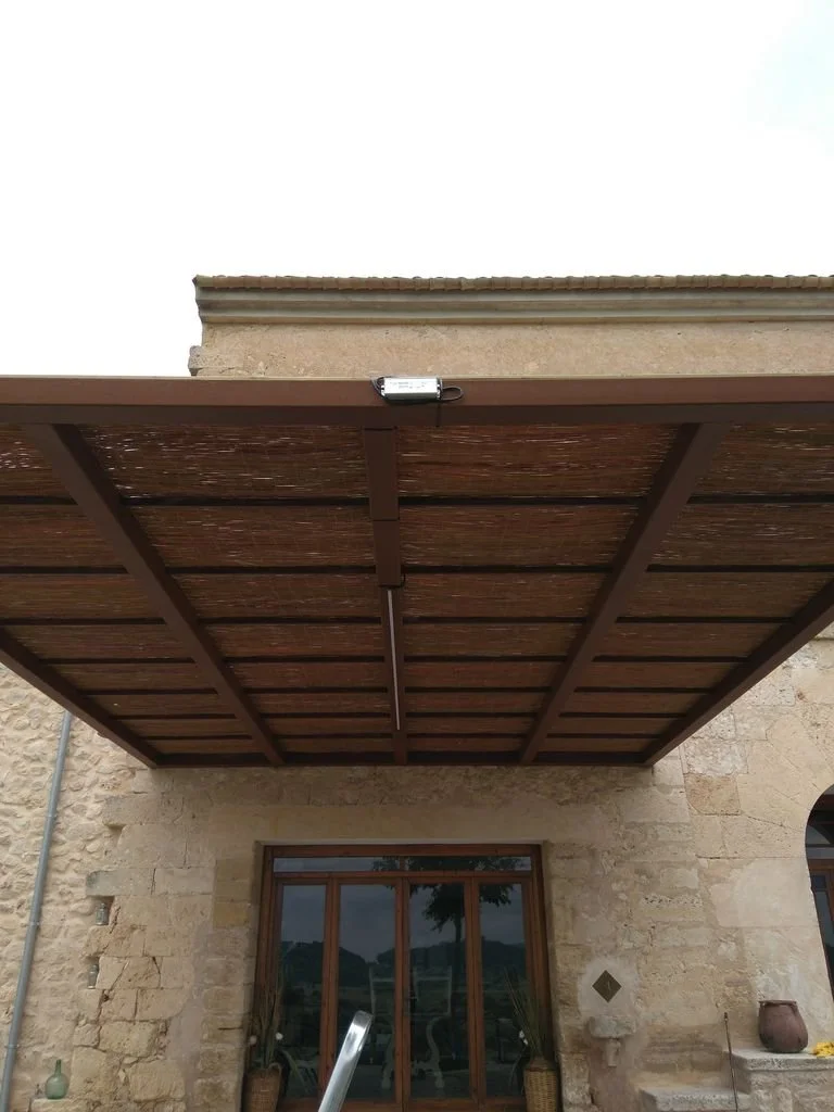Terraza de madera con un toldo en una casa de piedra y una ventana en la parte inferior.