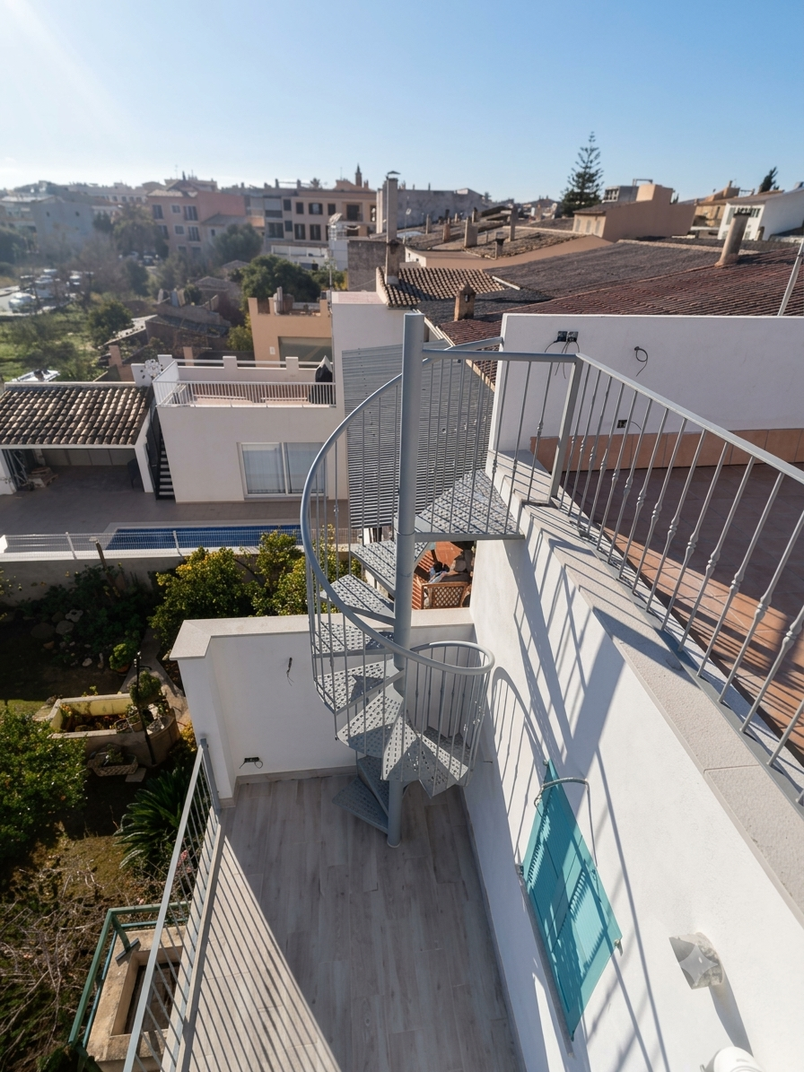 Vistas desde una azotea en una zona urbana, con una escalera de caracol de metal, barandillas blancas, edificios residenciales y un cielo despejado.