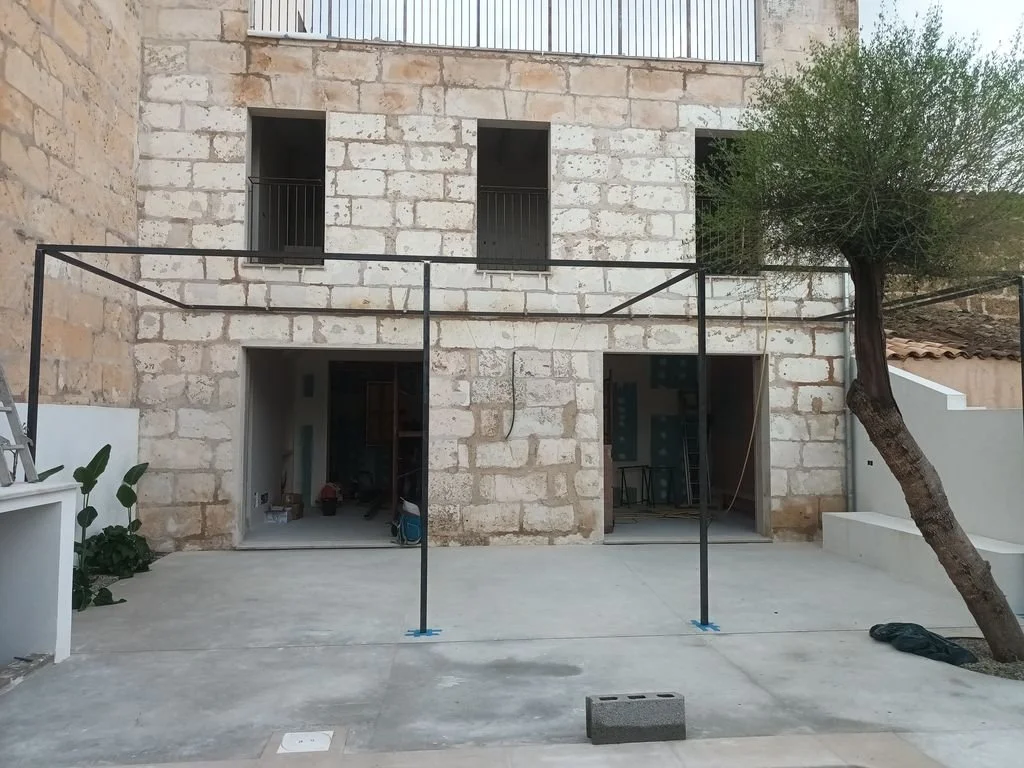 Construcción en proceso con estructura de metal en patio y árbol a la derecha