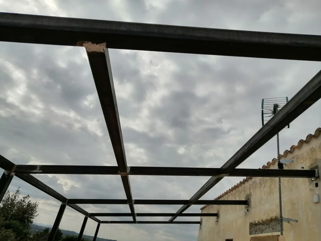 Estructura metálica para un cobertizo o porche en construcción, con cielo nublado de fondo.