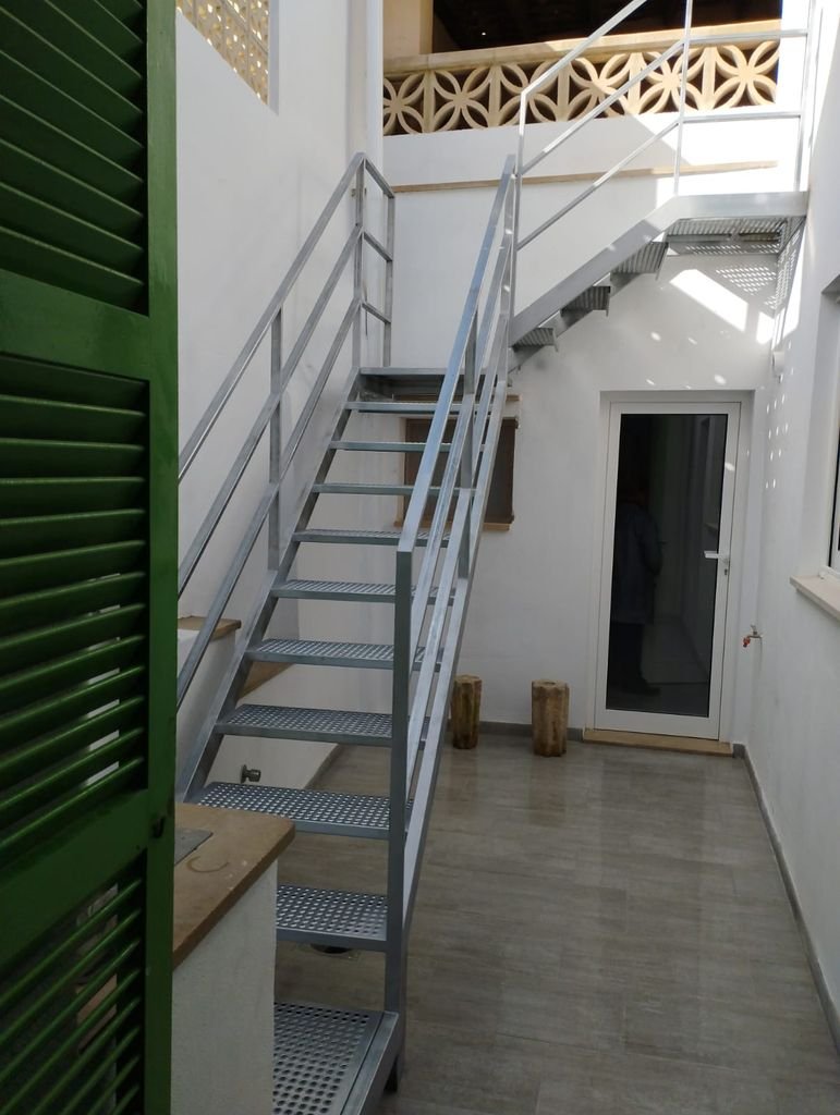 Escalera metálica exterior con pasamanos en un patio, con puerta de vidrio y pared blanca, en un entorno residencial.