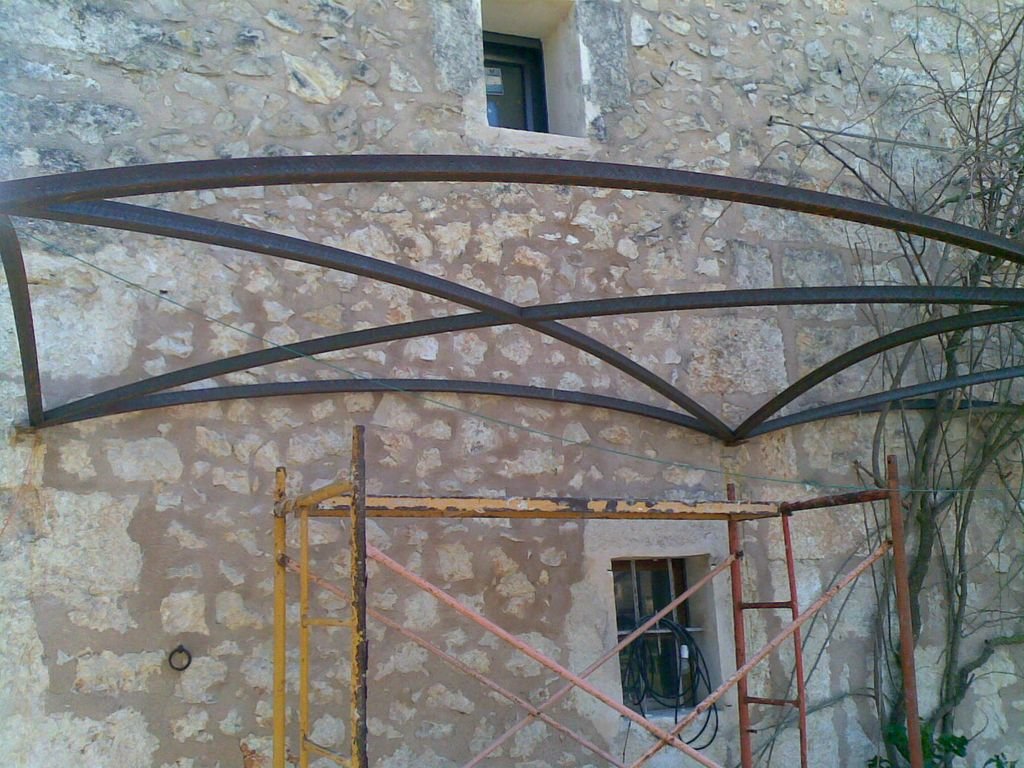 Conjunto de estructuras metálicas en proceso de instalación sobre una pared de piedra, con escaleras y andamios de construcción en un entorno exterior.
