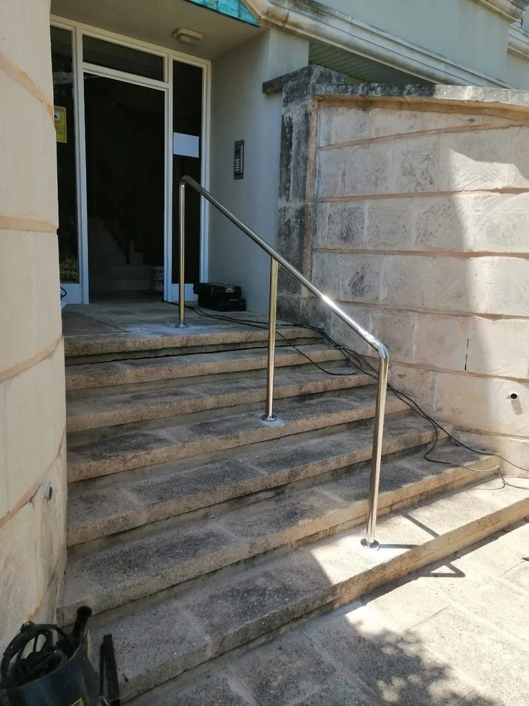 Escaleras de piedra a la entrada de un edificio con pasamanos de metal, cerca de la puerta principal 