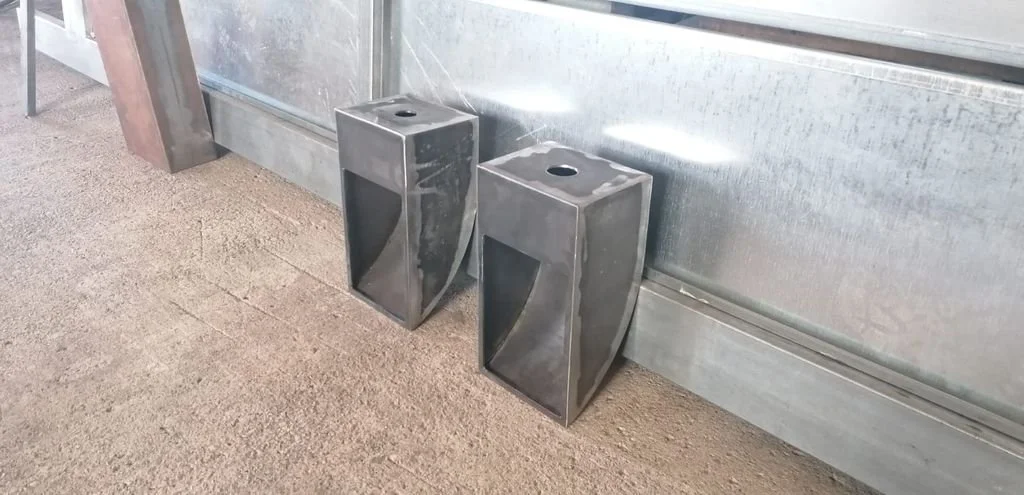 Dos coladeras de metal en el suelo, cerca de una pared metálica, en un área que parece ser industrial o de construcción.